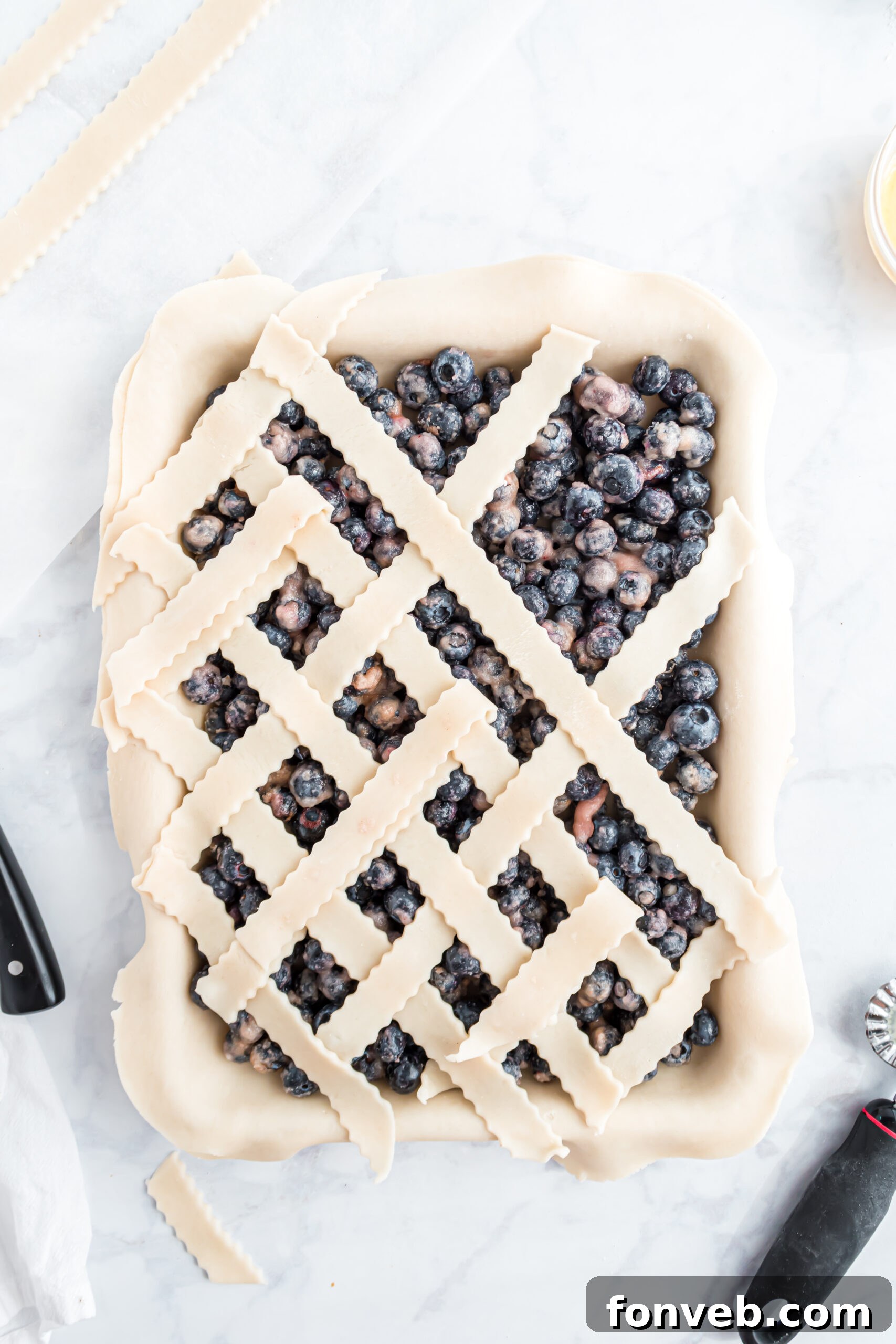 A detailed photo demonstrating the intricate steps to expertly add the lattice topping onto the blueberry pie.