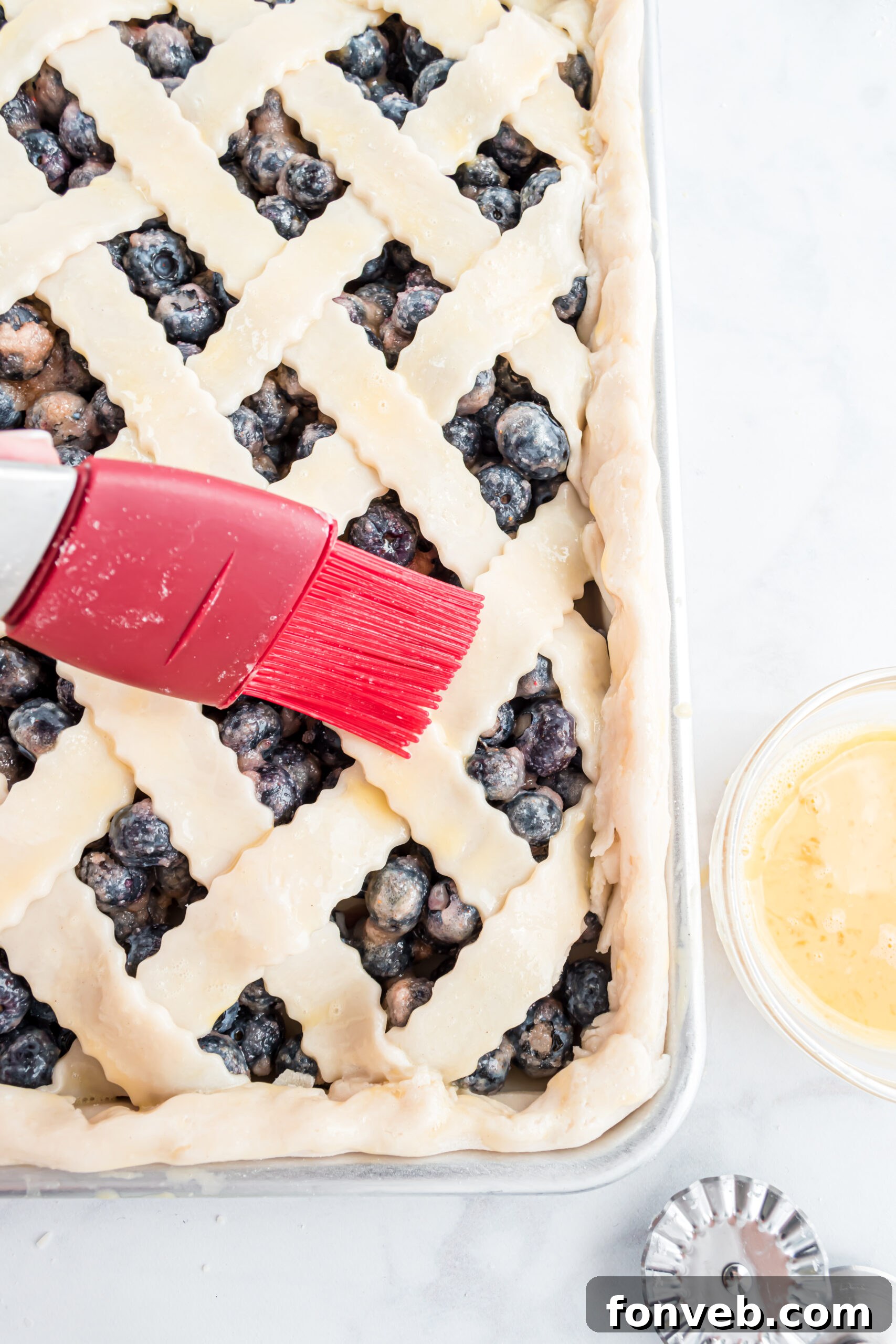 The final touch: gracefully brushing egg wash onto the top lattice crust of the pie, ensuring a golden finish.
