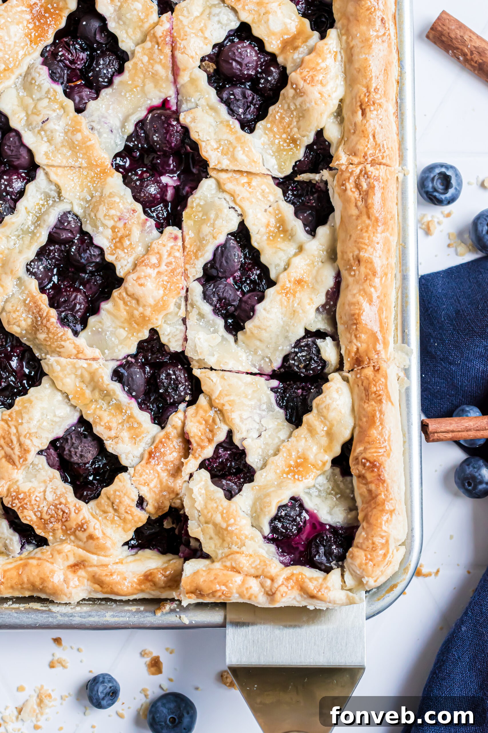 A perfectly baked piece of blueberry pie being carefully lifted from the pan with a silver and wooden spatula, showcasing its golden crust.