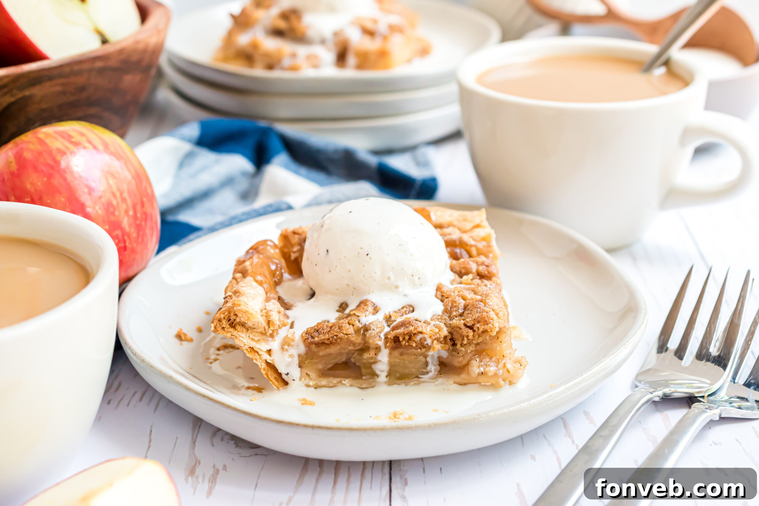 A piece of apple pie on a white plate with a silver fork topped with vanilla ice cream. 