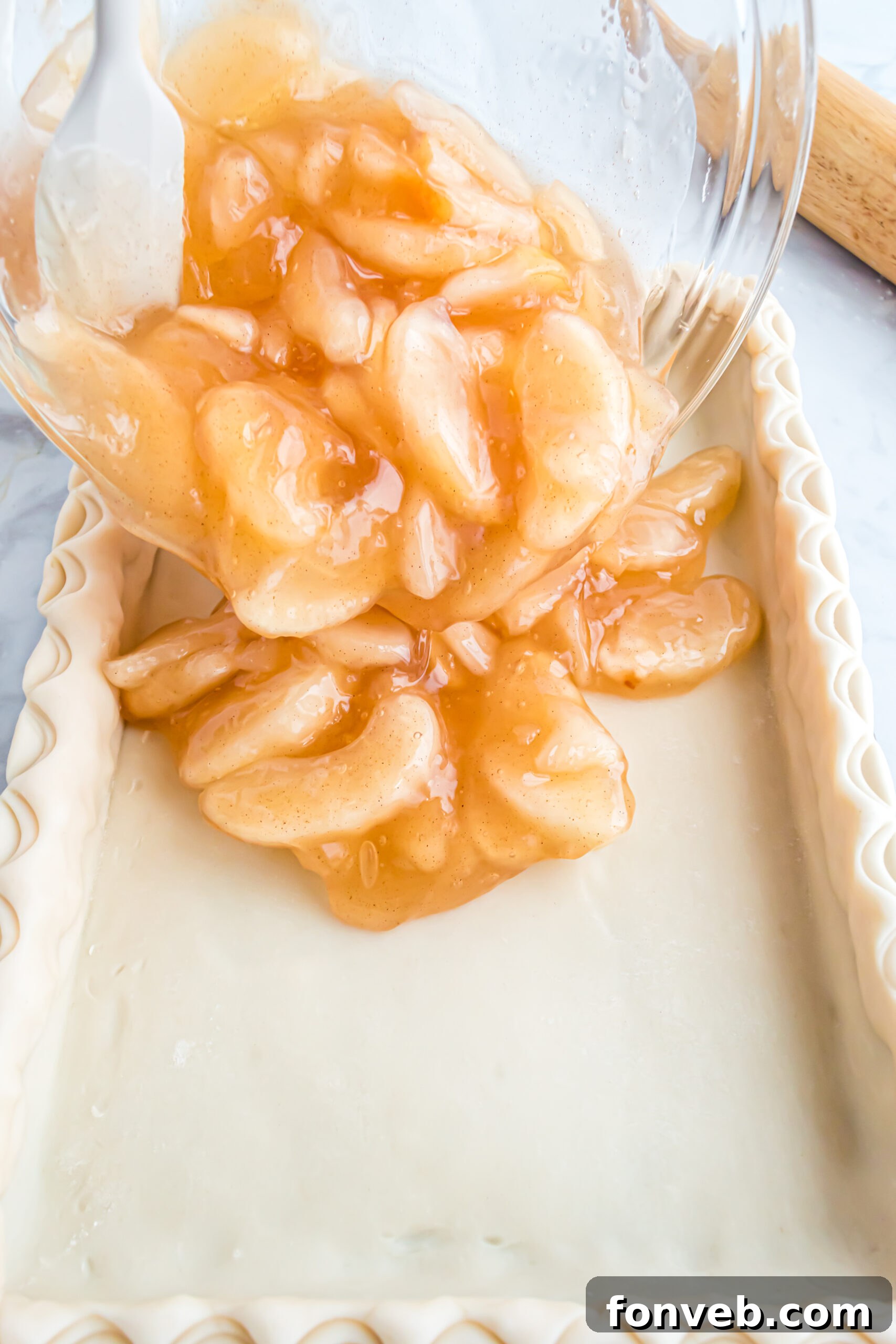 Pouring the apple pie filing into the prepared crust. 