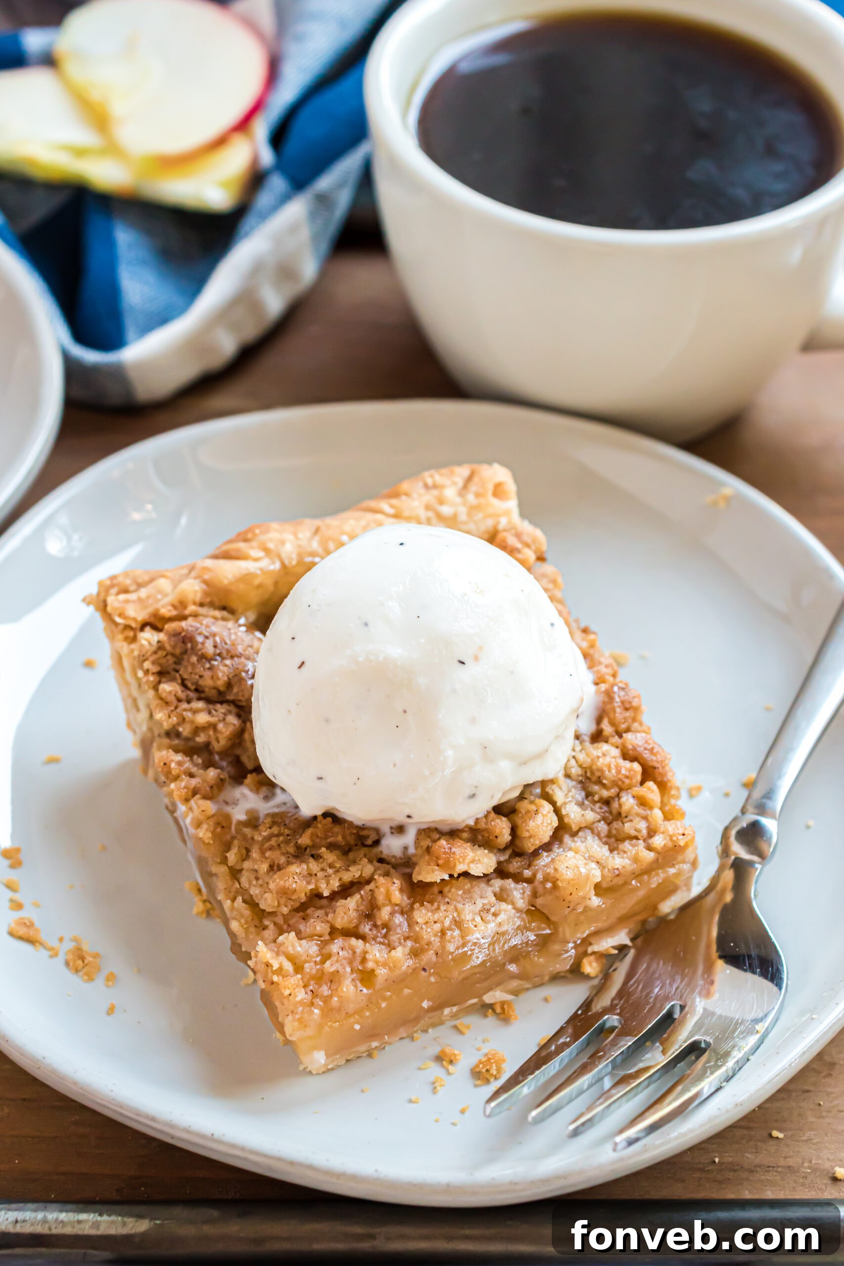 A piece of apple pie on a white plate with a silver fork topped with vanilla ice cream. 