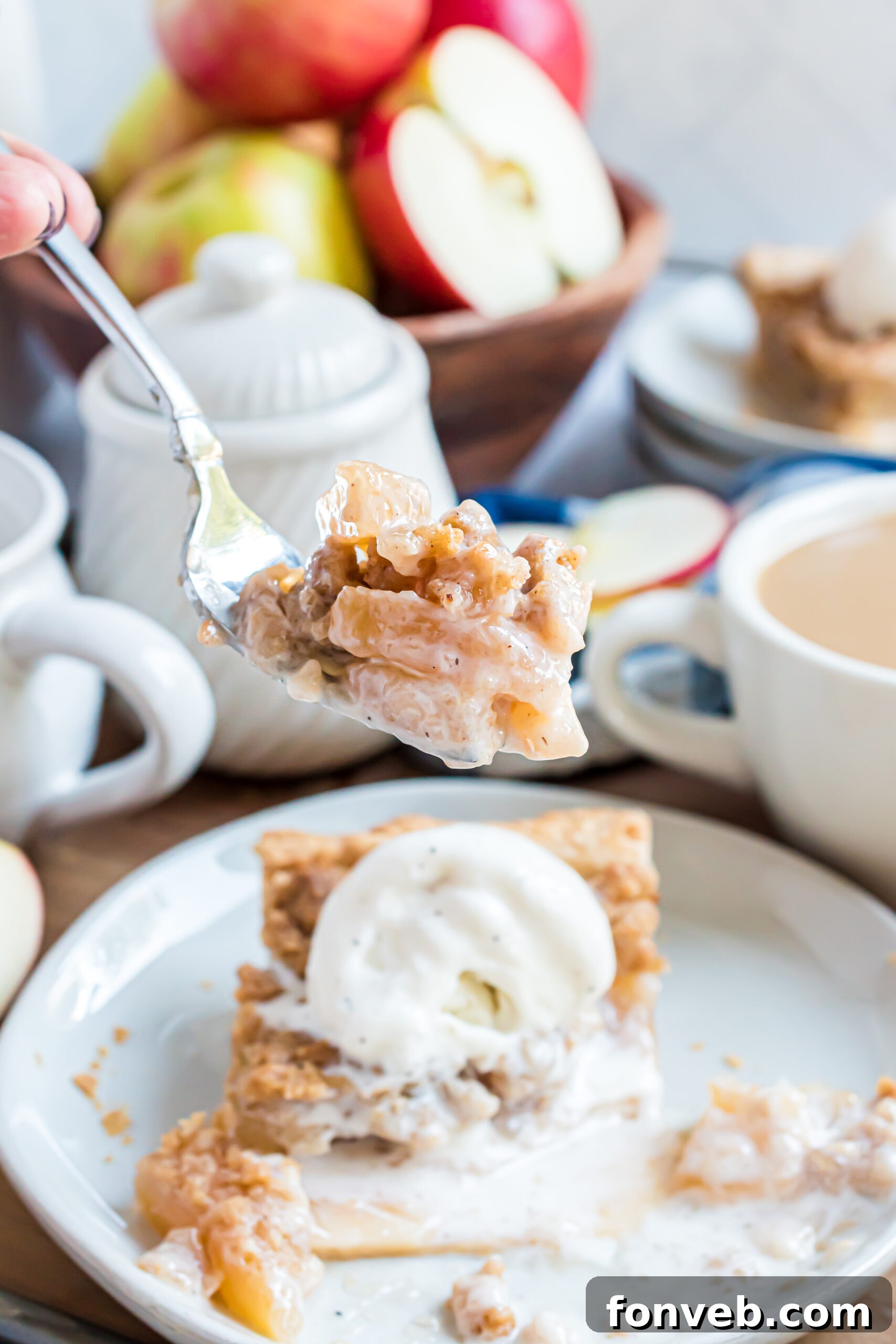 A piece of apple pie on a white plate with a silver fork removing a bite and topped with vanilla ice cream. 