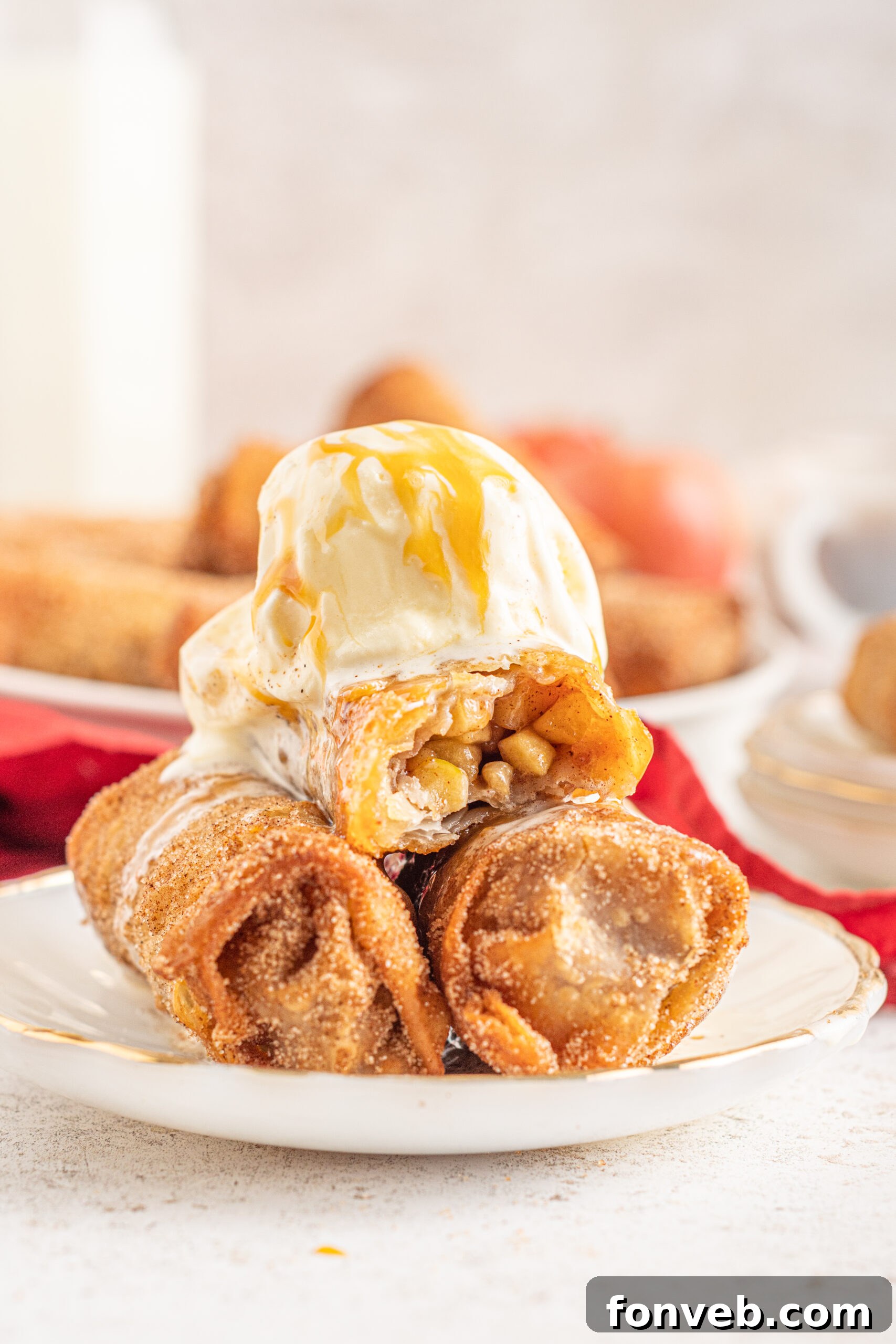 Three Apple Pie Egg Rolls stacked on a white plate with ice cream and caramel sauce on top. 