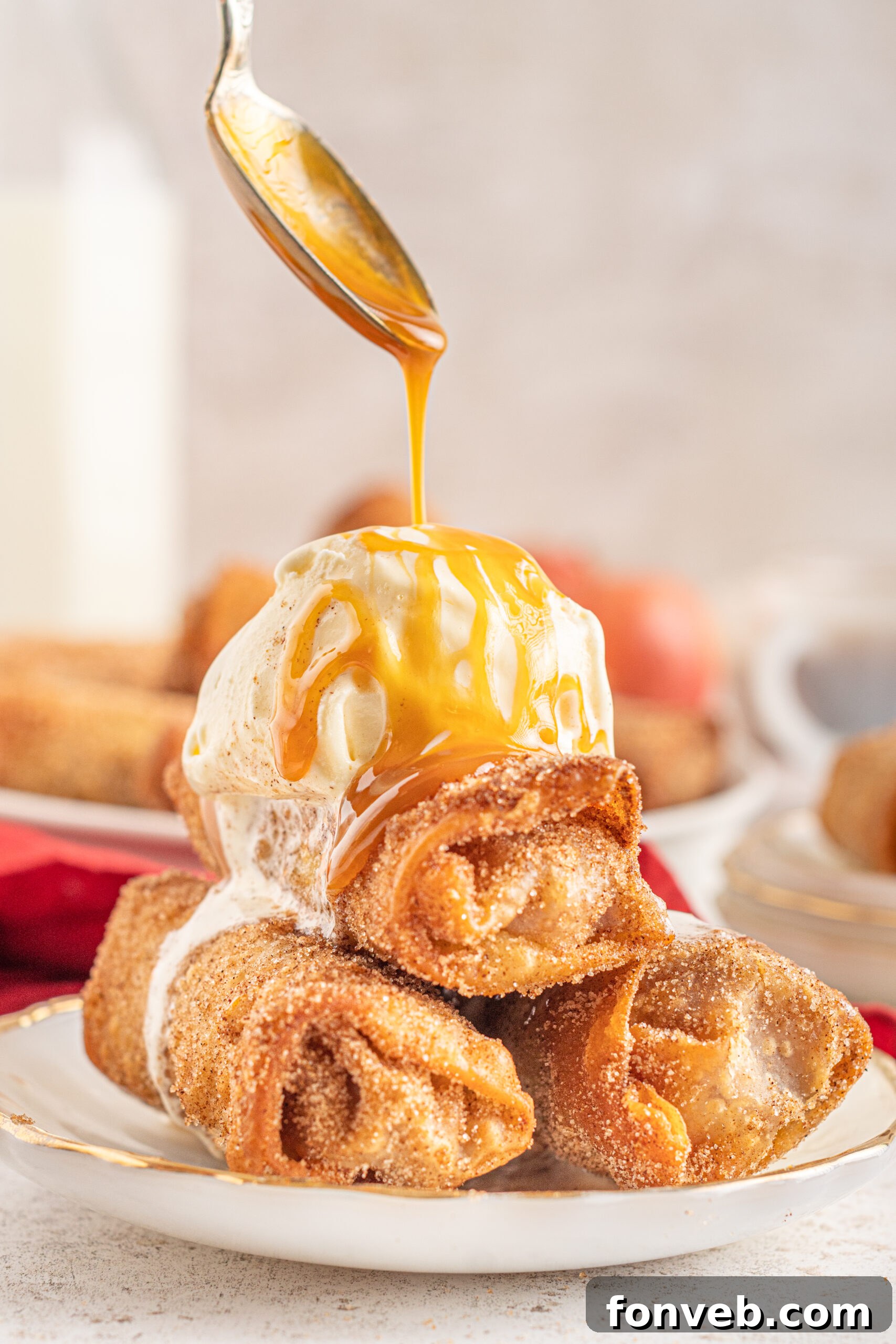 Three Egg Rolls stacked on a white plate with ice cream and caramel sauce on top. 