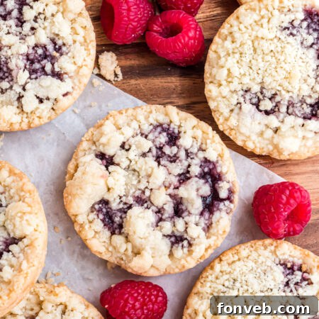 Freshly baked raspberry cookies on wax paper with fresh raspberries, ready to be enjoyed or stored.