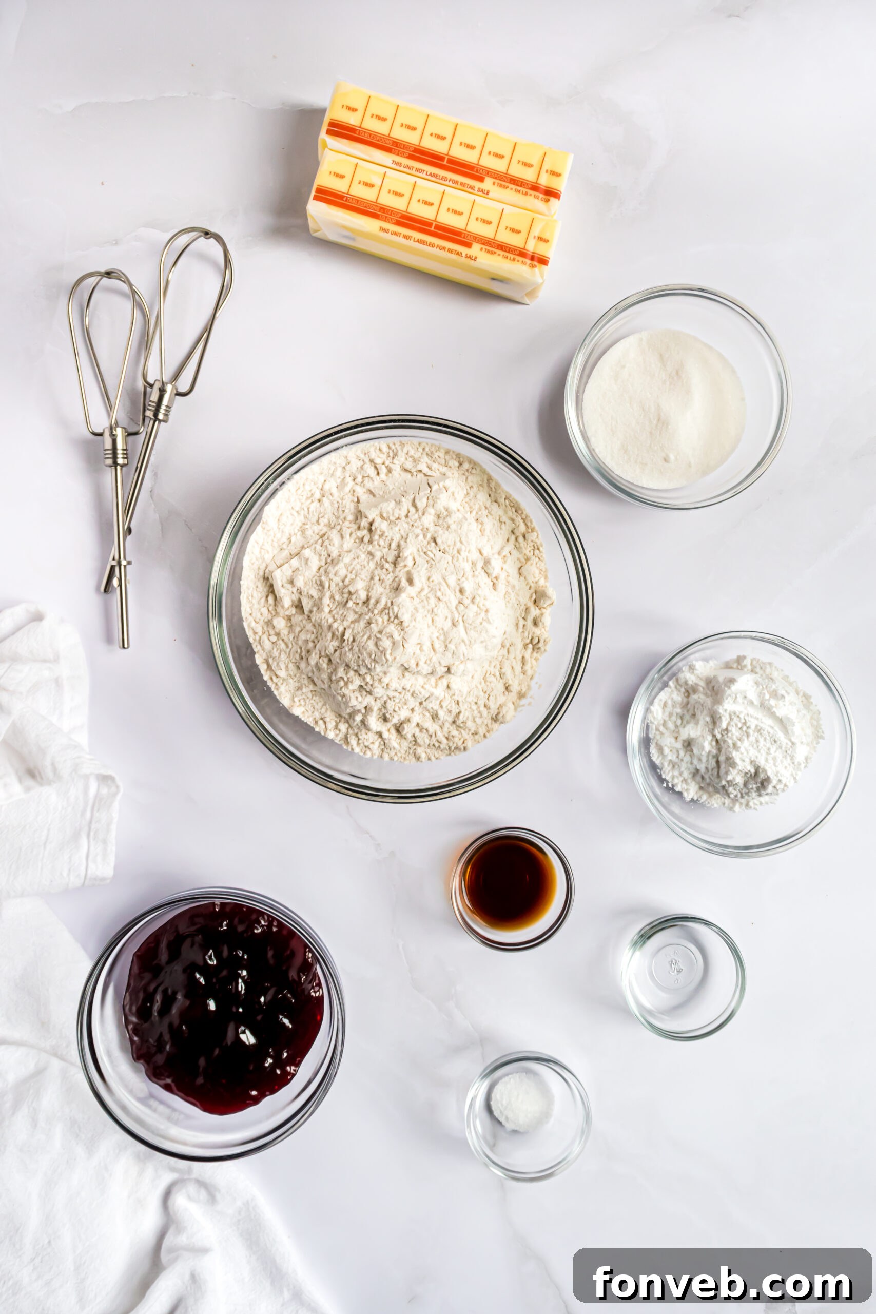 An overhead shot of all the essential ingredients laid out neatly on a surface, including butter, sugars, extracts, flour, and raspberry jam, ready for baking.