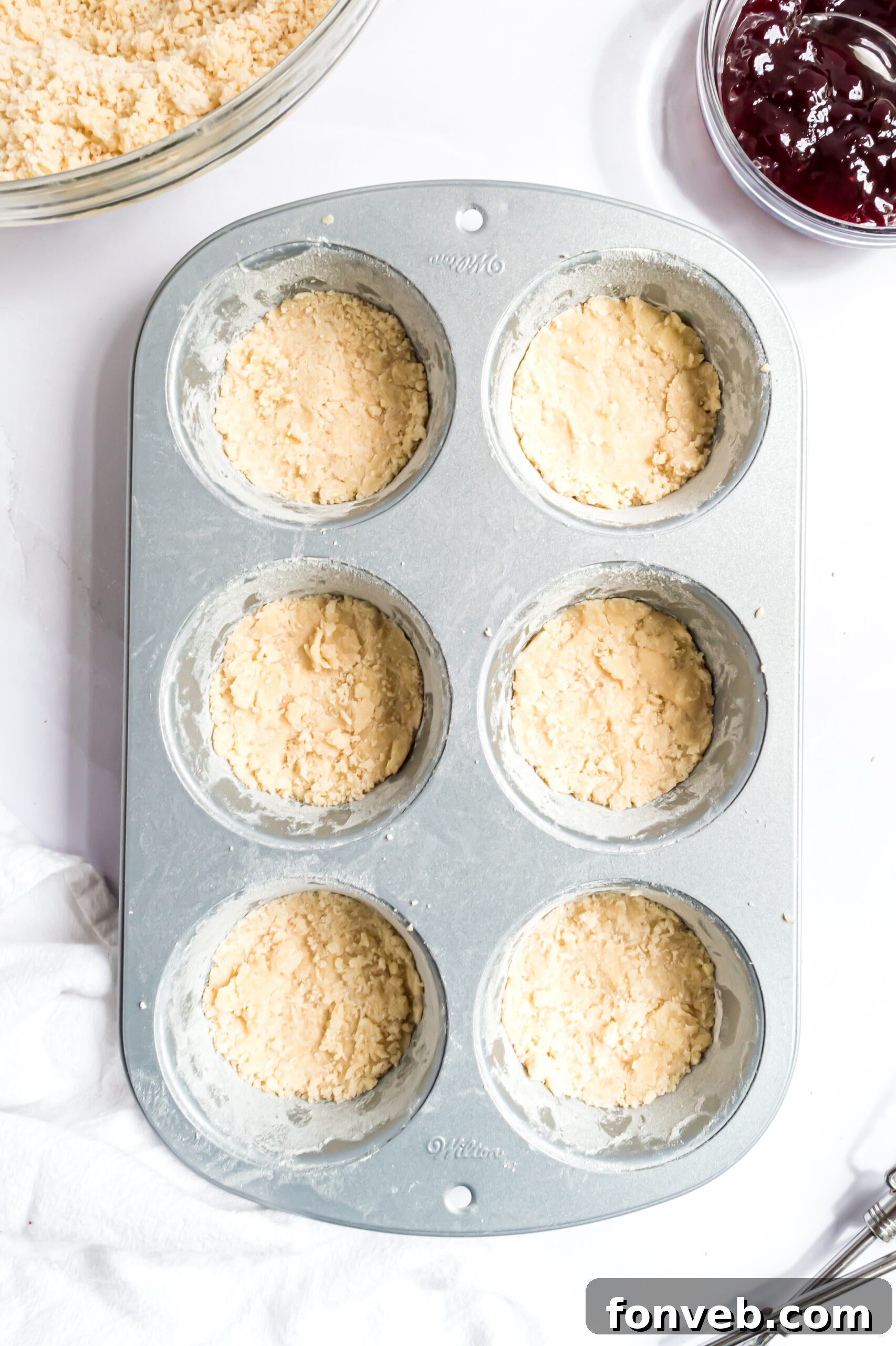 An overhead shot showing the buttery cookie crust expertly pressed into the individual wells of a muffin tin, ready for filling.