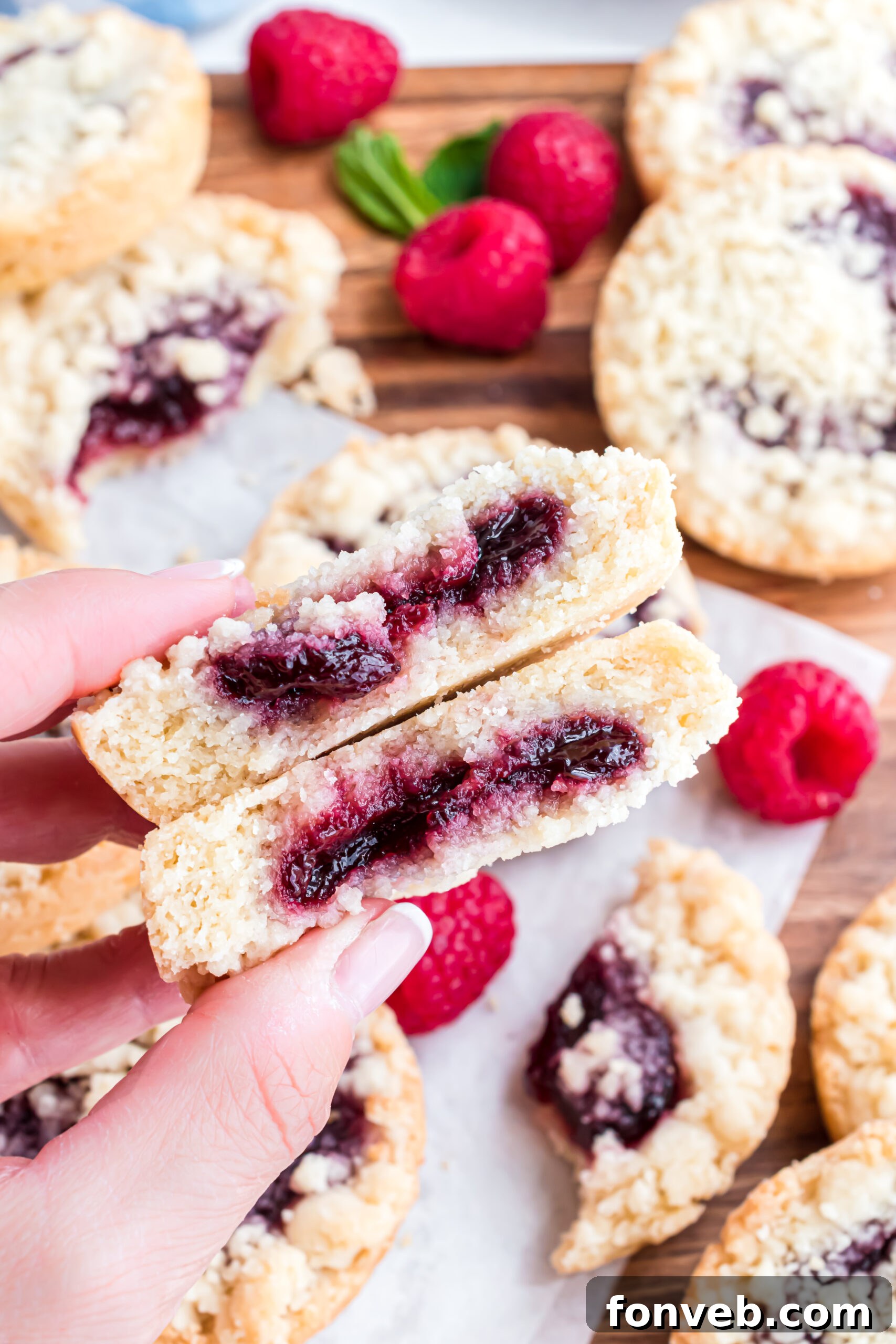 A perfectly baked raspberry cookie, neatly sliced in half, vividly displaying the rich, glistening raspberry jam filling at its core and the crumbly texture of the cookie and topping.