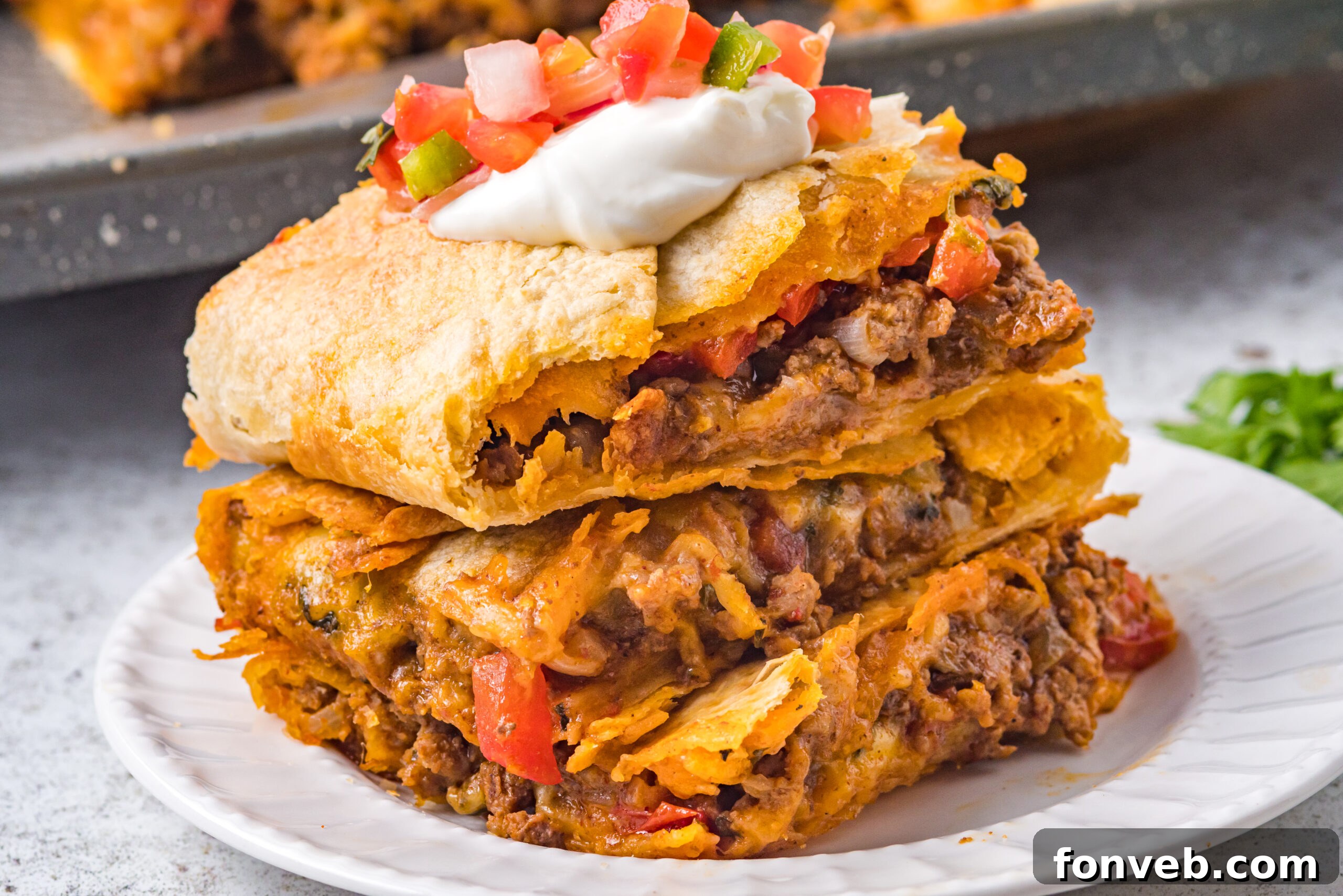 One Pan Baked Tacos 13 Stacked sheet pan tacos resting on a clean white plate, artfully garnished with a generous dollop of sour cream and a colorful topping of Pico de Gallo