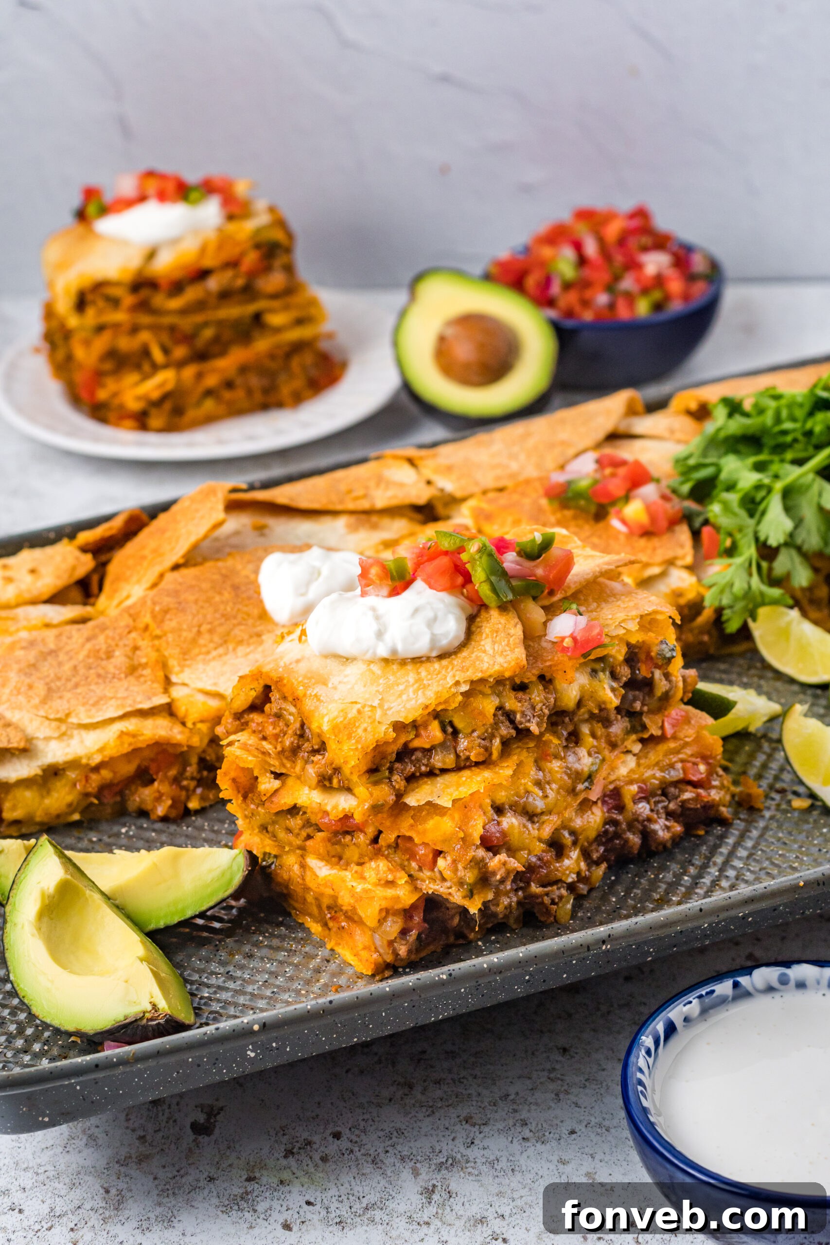 One Pan Baked Tacos 3 Three slices of perfectly baked sheet pan tacos stacked on a baking sheet, generously topped with fresh sour cream and vibrant Pico de Gallo