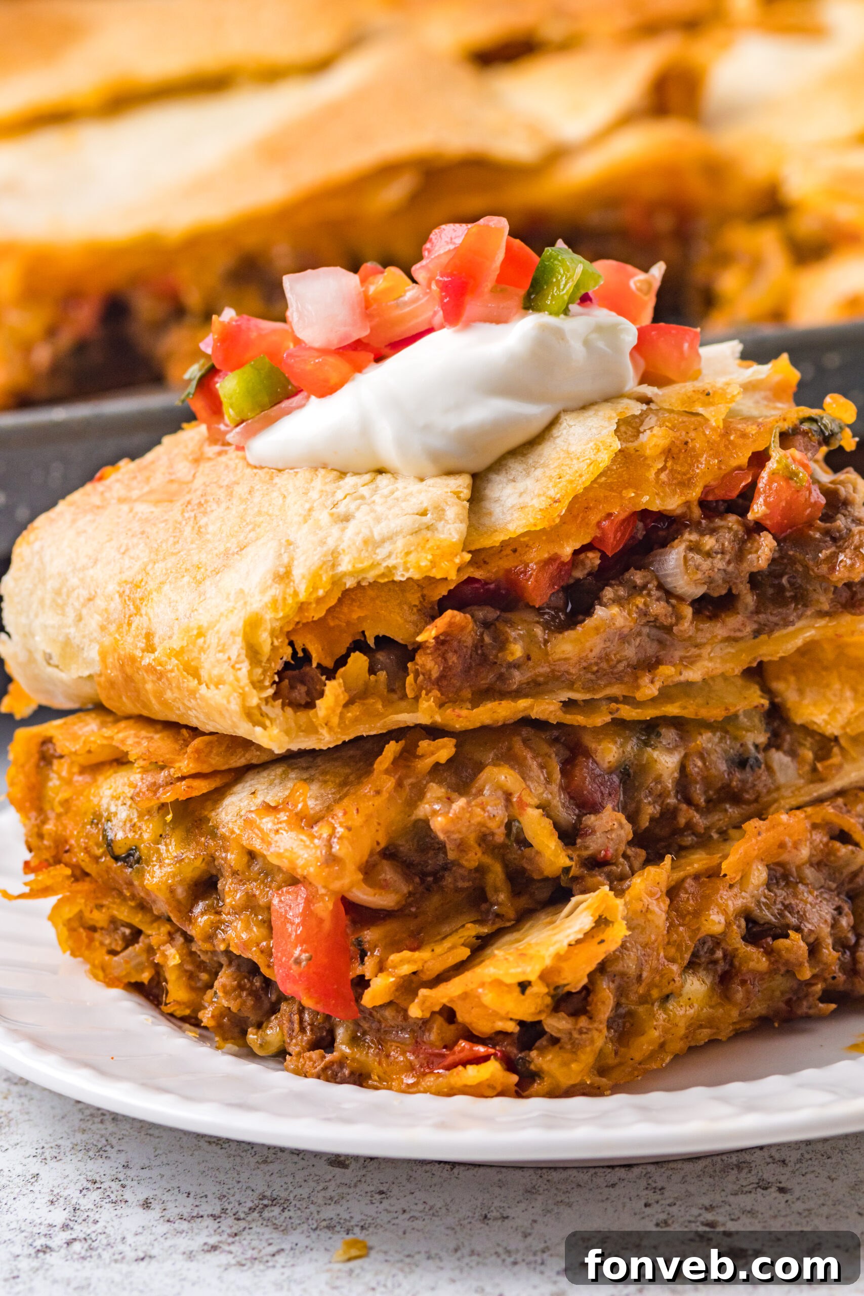 One Pan Baked Tacos 4 Three slices of golden-brown sheet pan tacos neatly stacked on a crisp white plate, adorned with a colorful and fresh Pico de Gallo topping
