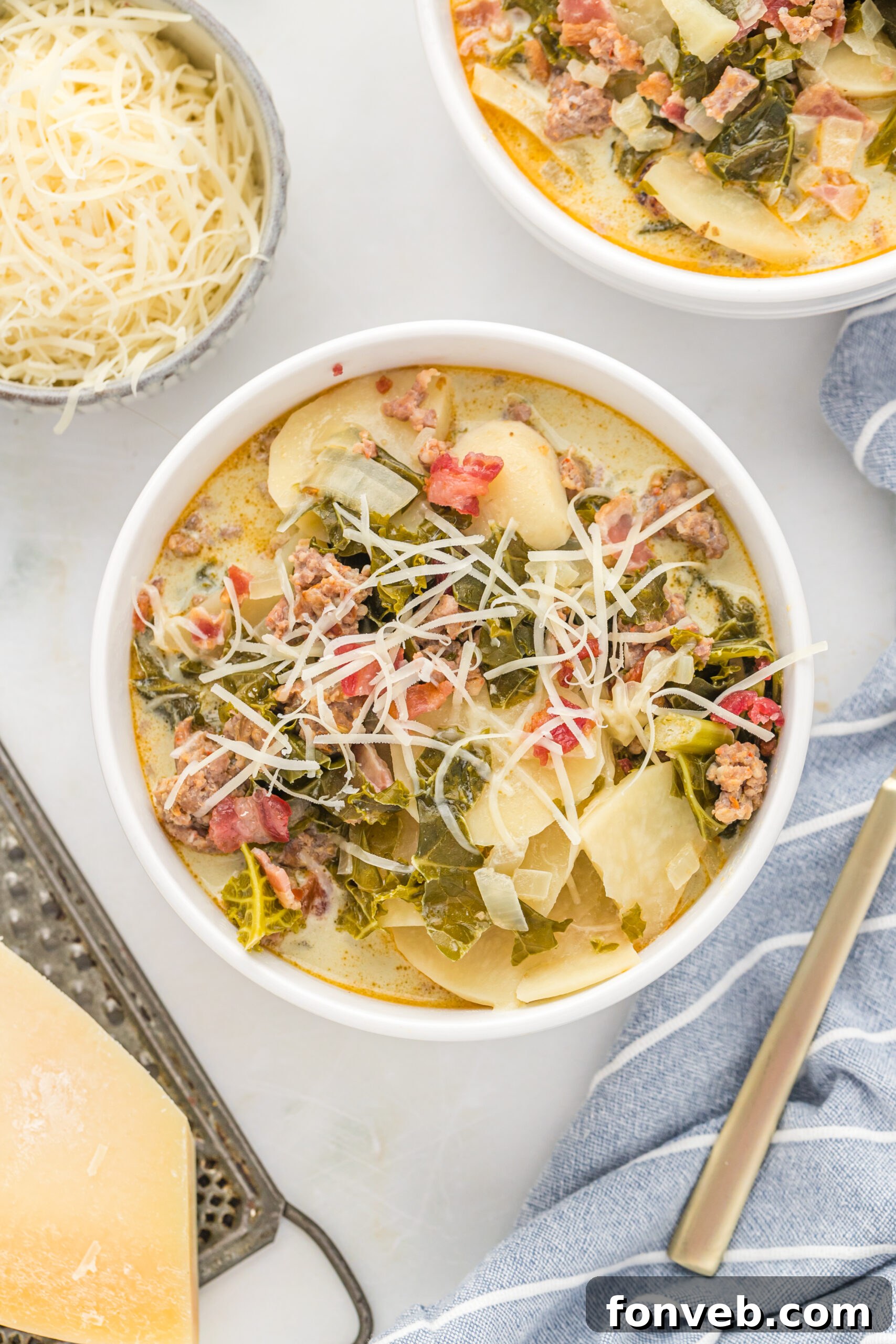 Overhead view of the soup in white bowls topped with shredded cheese with a blue and white stripped linen in the background. 