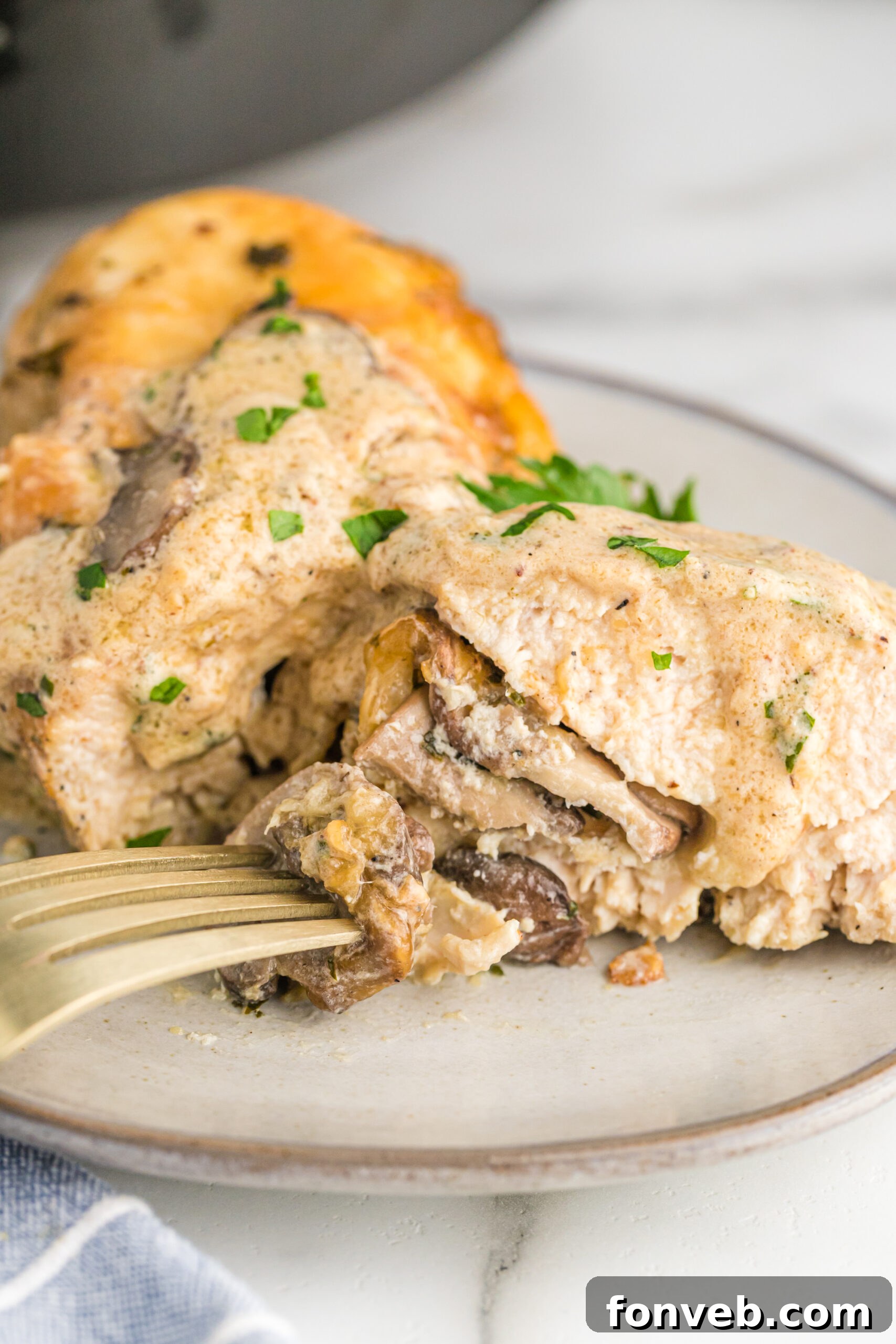 Garlic Butter Chicken Stuffed with Cheesy Mushrooms 11 A close-up of a cooked piece of Cheesy Garlic Butter Mushroom Stuffed Chicken cut in half, clearly showing the luscious stuffing within.