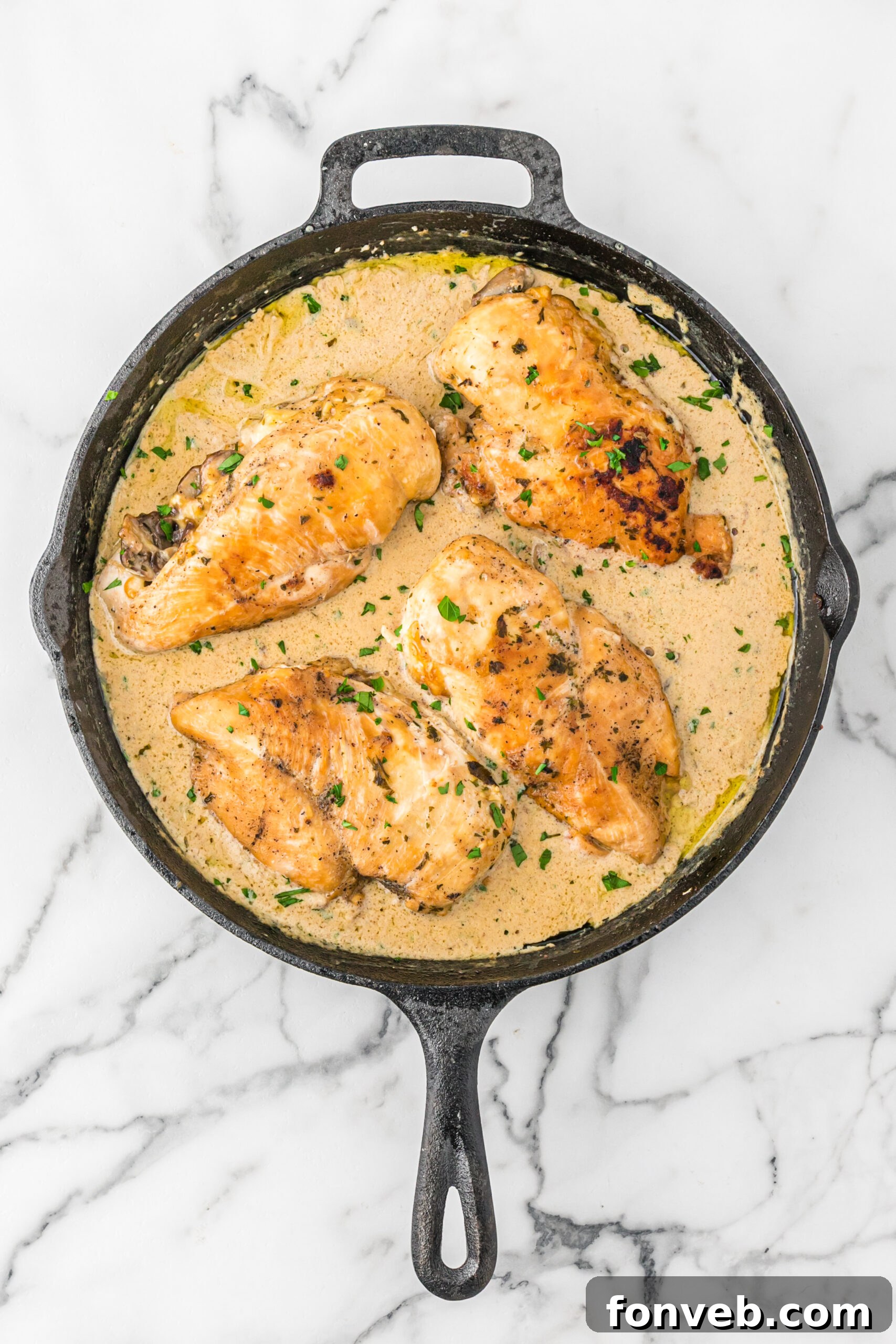 Garlic Butter Chicken Stuffed with Cheesy Mushrooms 5 Overhead view of Cheesy Garlic Butter Mushroom Stuffed Chicken baking in a cast iron skillet, showing golden-brown chicken and bubbling sauce.