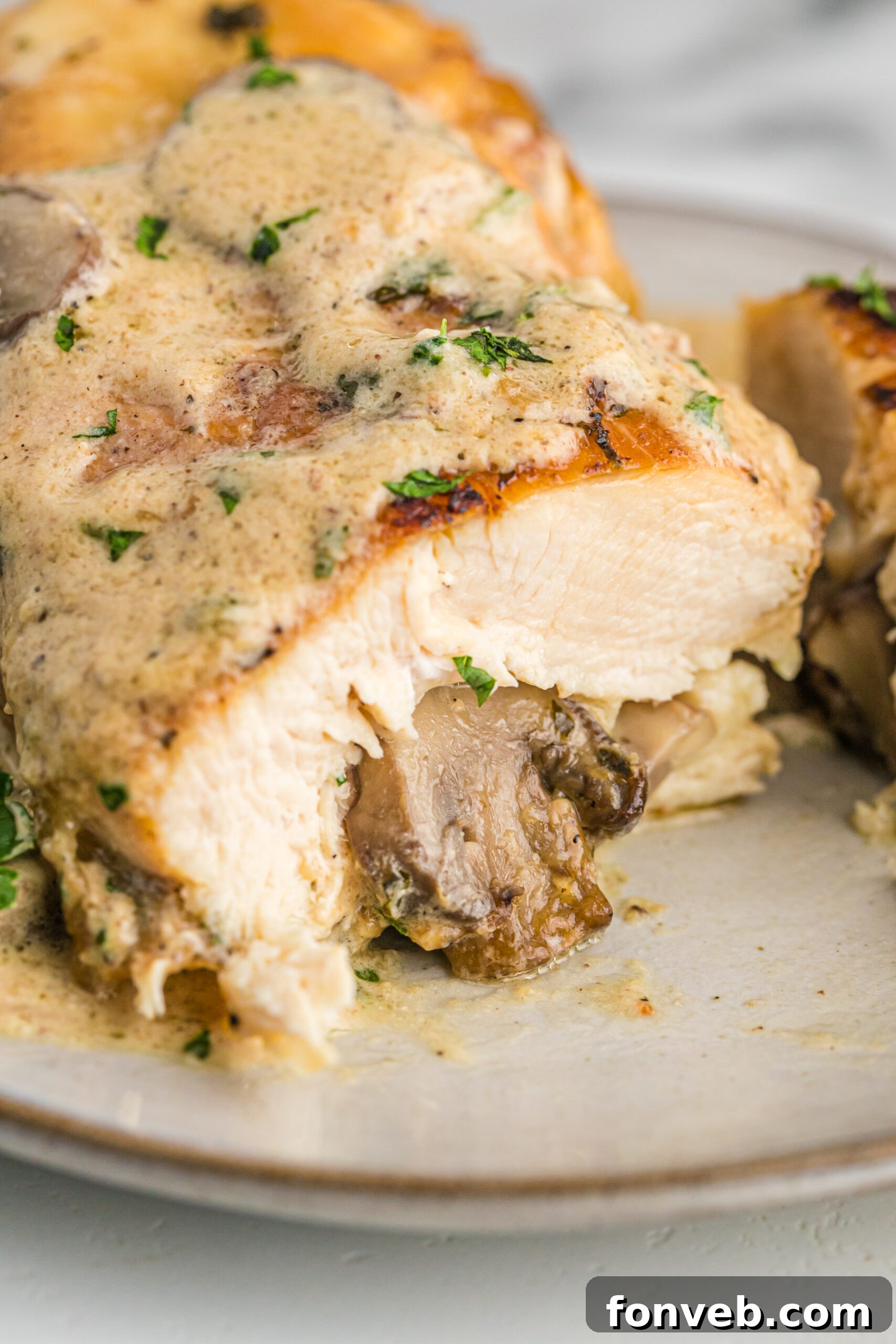 Garlic Butter Chicken Stuffed with Cheesy Mushrooms 9 A close-up of a cooked piece of Cheesy Garlic Butter Mushroom Stuffed Chicken cut in half, revealing the creamy, cheesy mushroom stuffing inside.