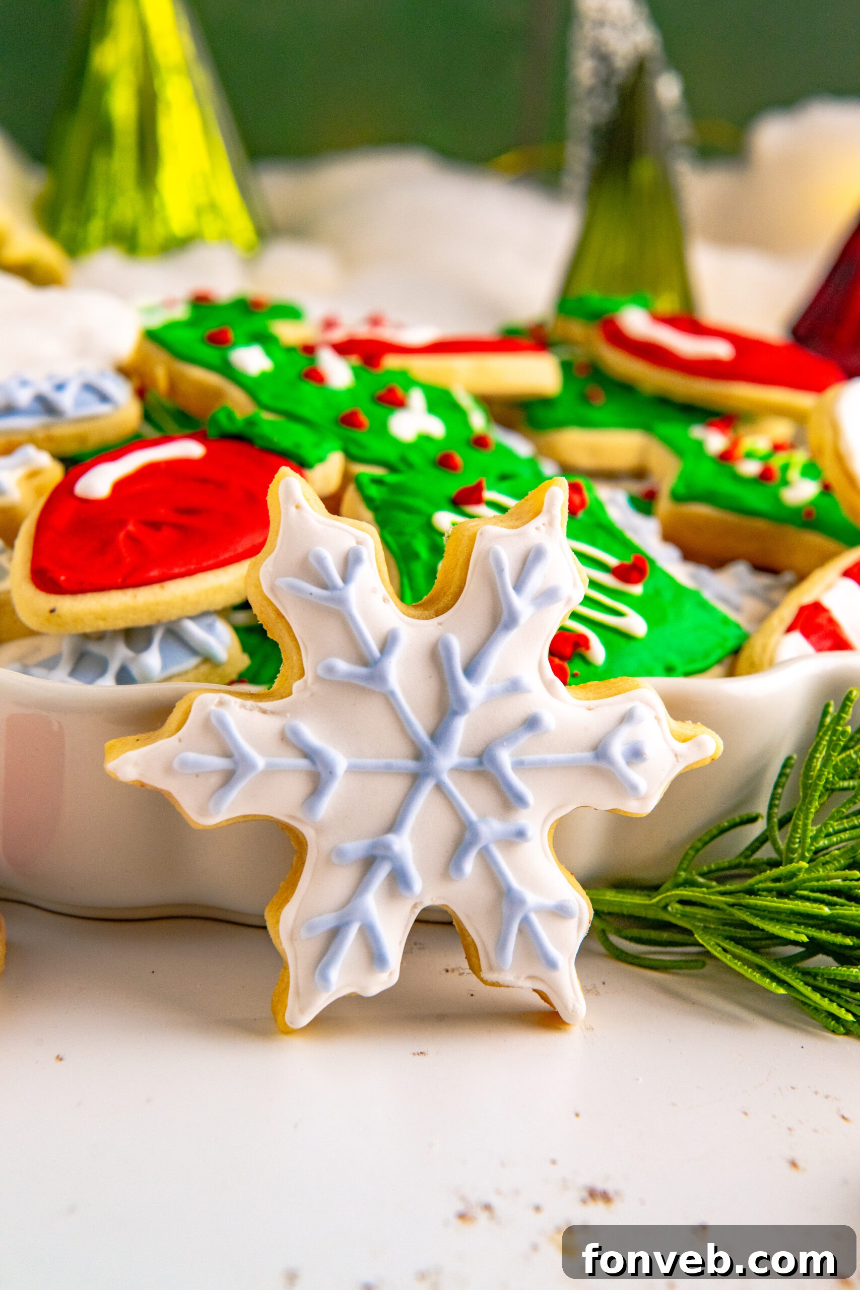 A white and light blue star cookie propped against a white serving tray stacked with Christmas cookies.