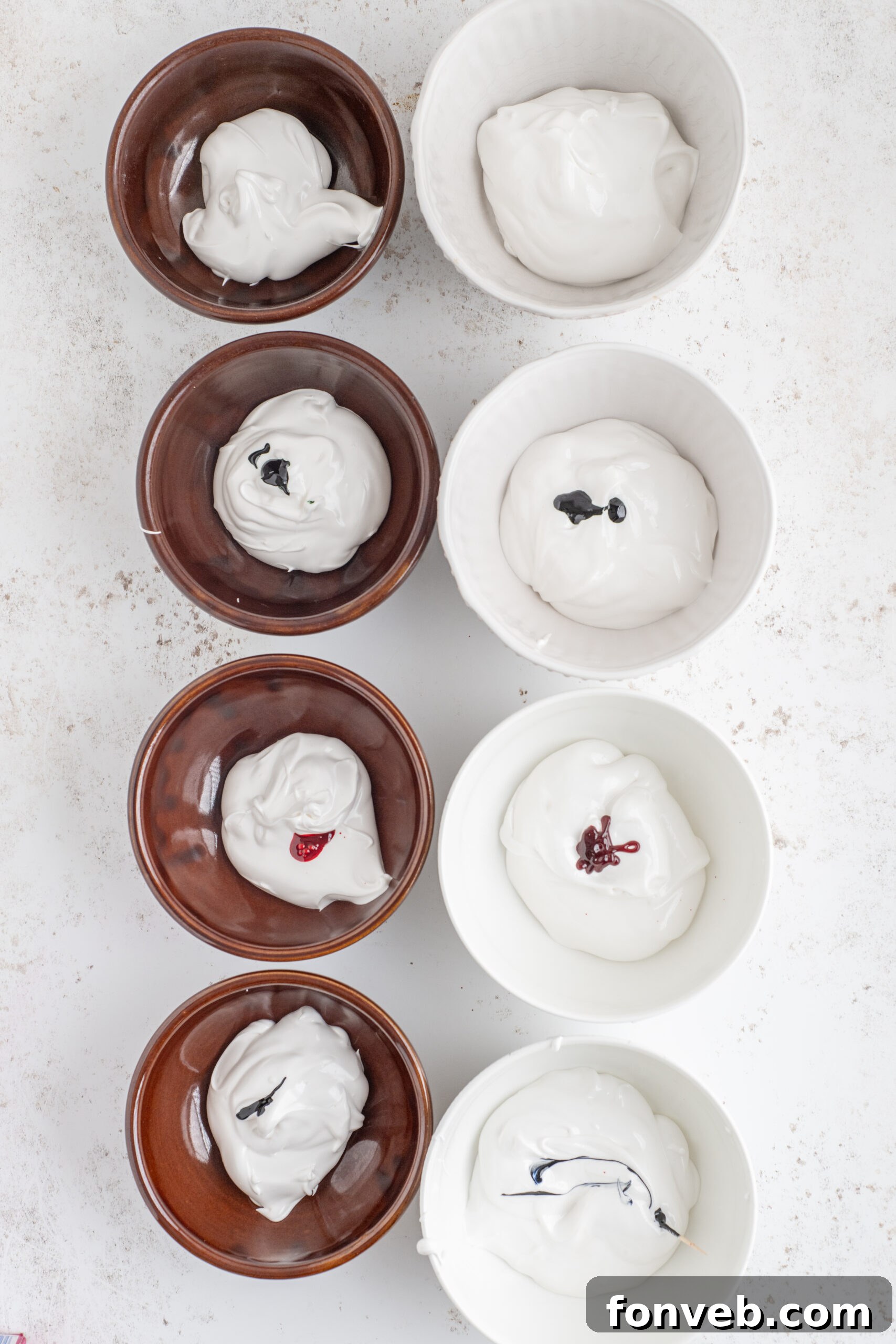 Above shot of the icing in 8 smaller bowls with food coloring added.
