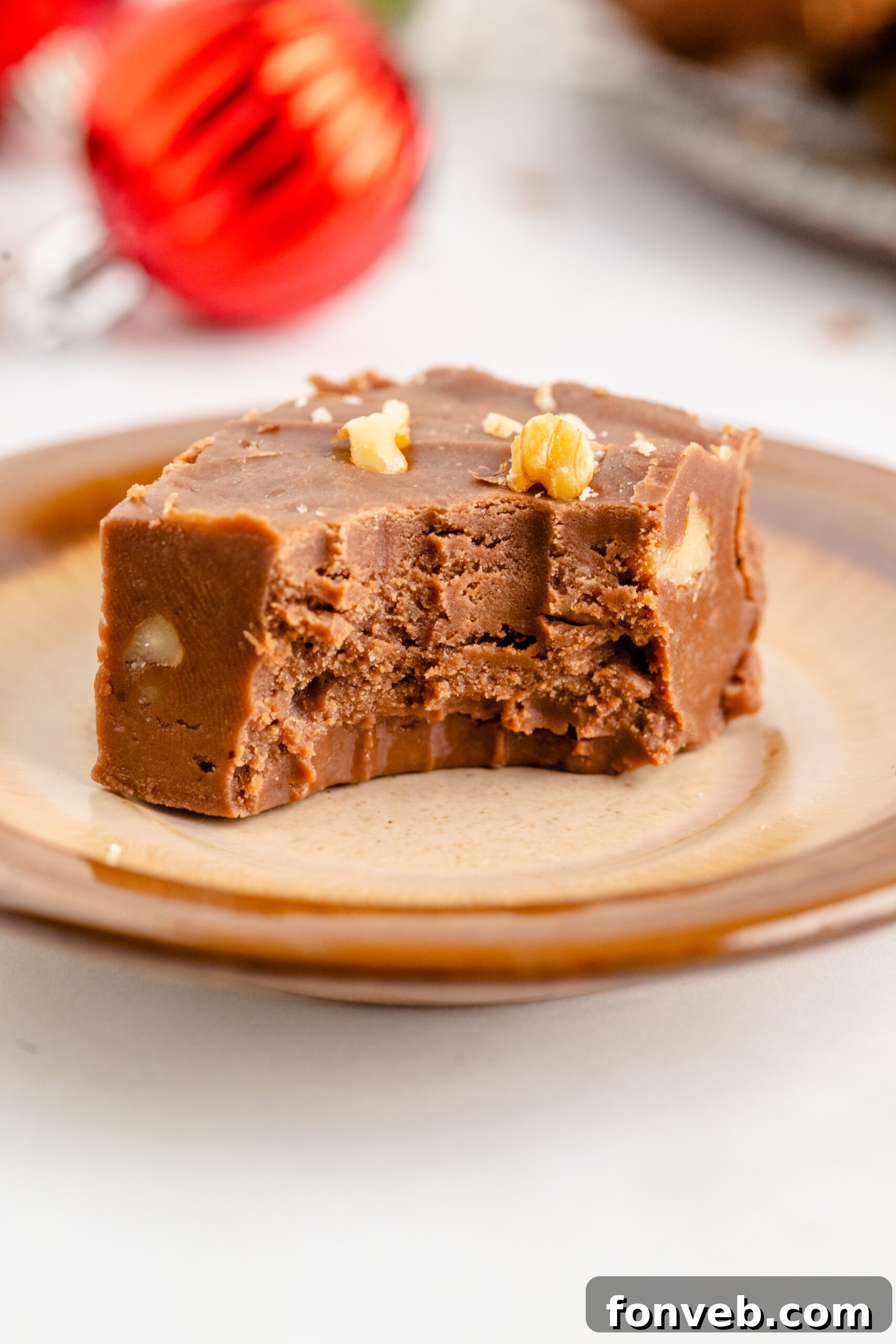 A piece of fantasy fudge on a brown plate with a bite removed showing the inside. 