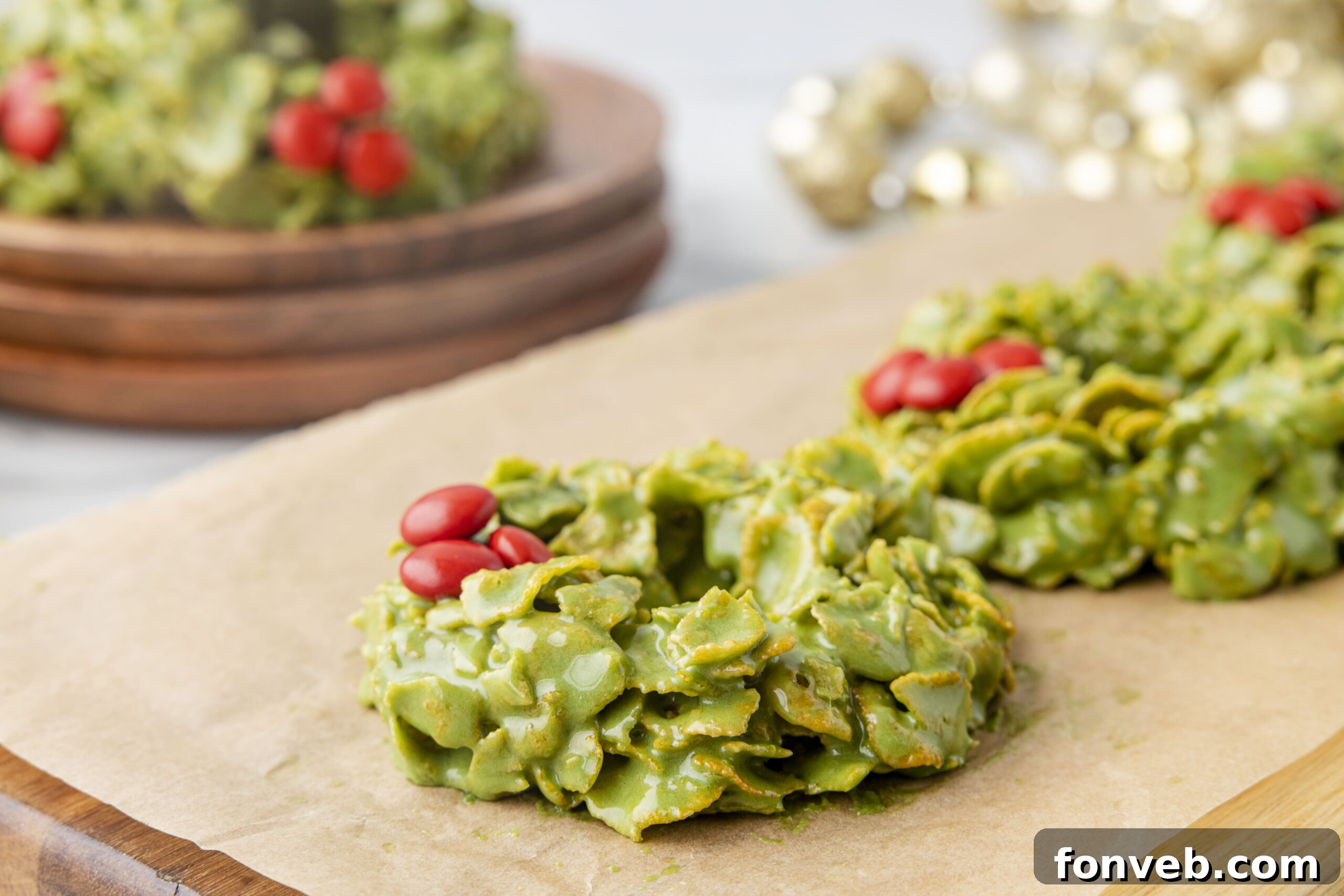 Side view of two finished cornflake wreaths, one with M&M's and one with red hot candies, on parchment paper.