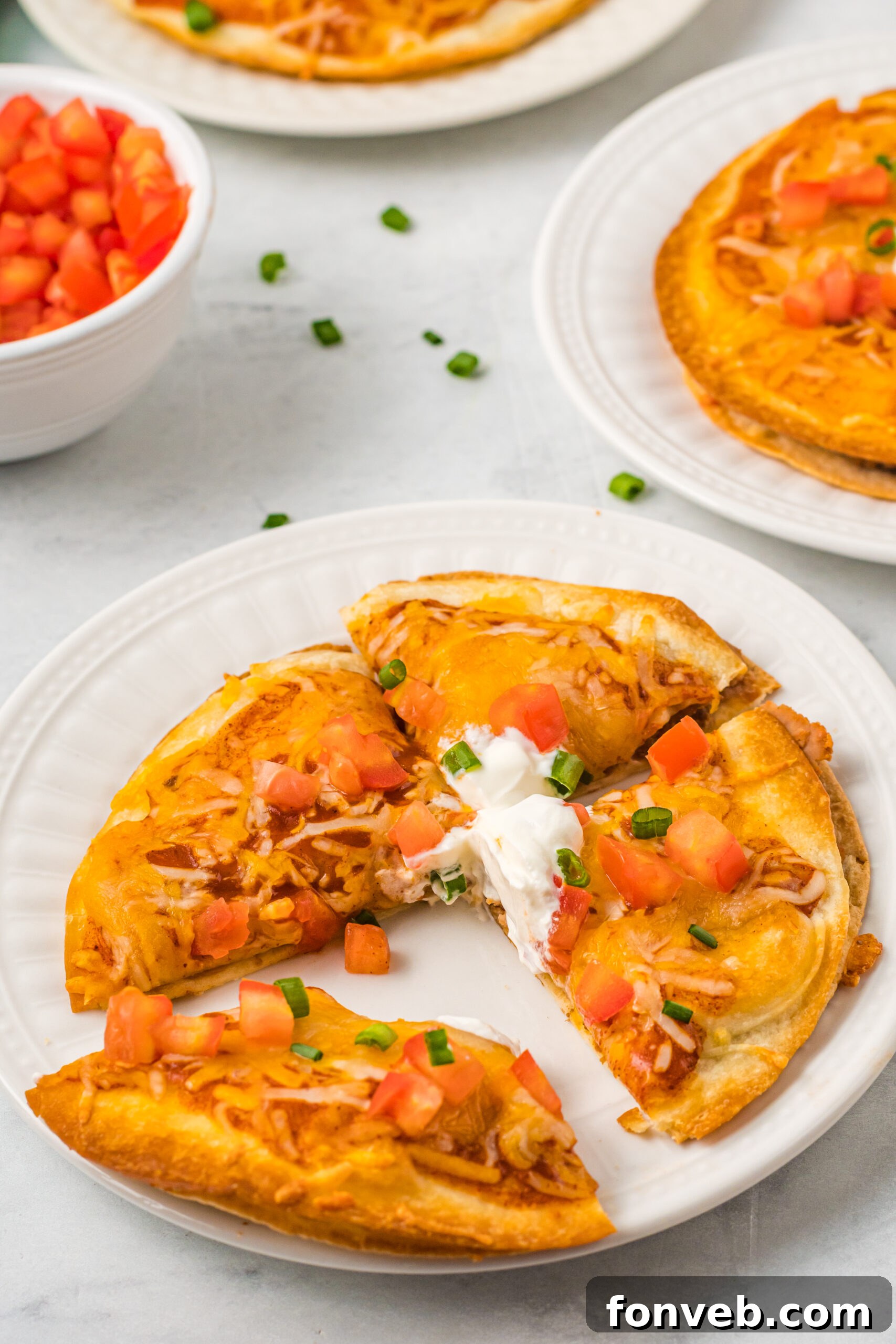 Mexican Pizza on a white plate cut into quarters topped with sour cream, tomatoes, and green onion. 