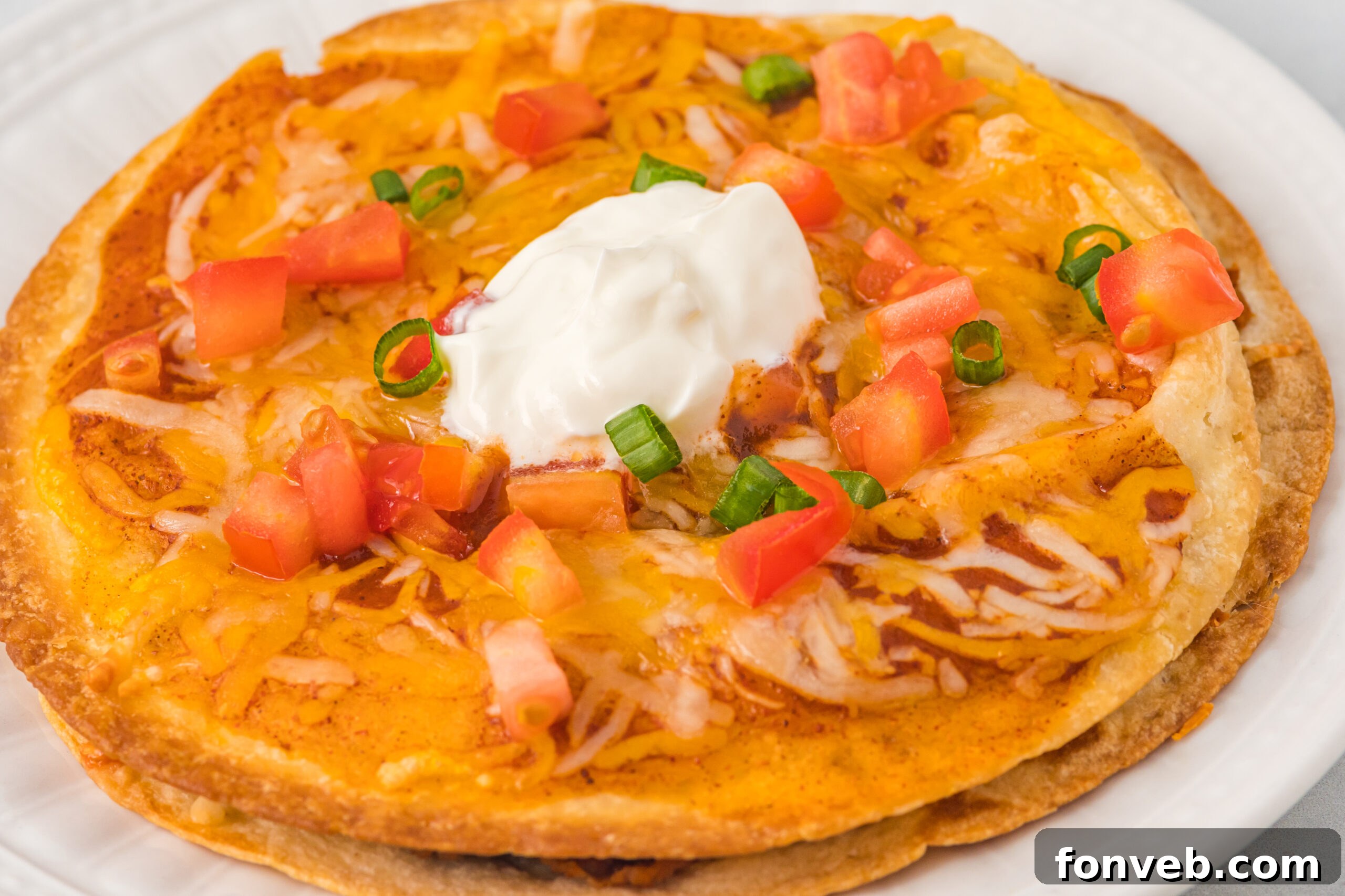 Up close photo of a mexican pizza topped with sour cream, tomatoes and green onions