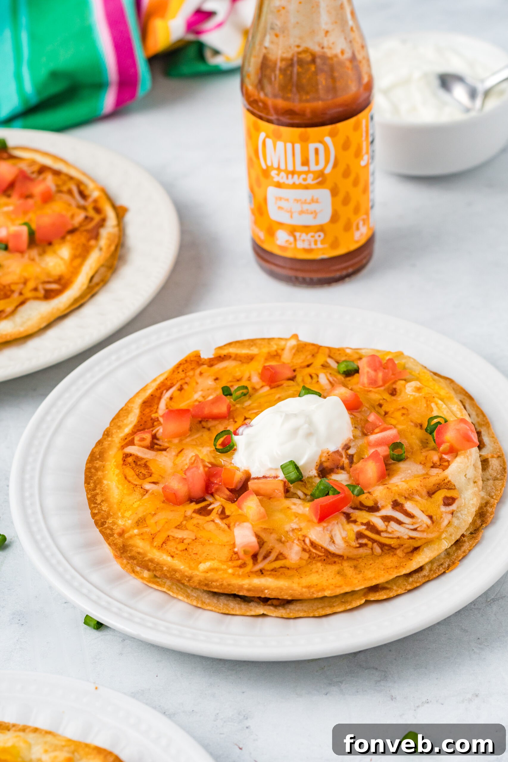 Mexican Pizza on a white plate topped with sour cream, tomatoes, and green onion. 
