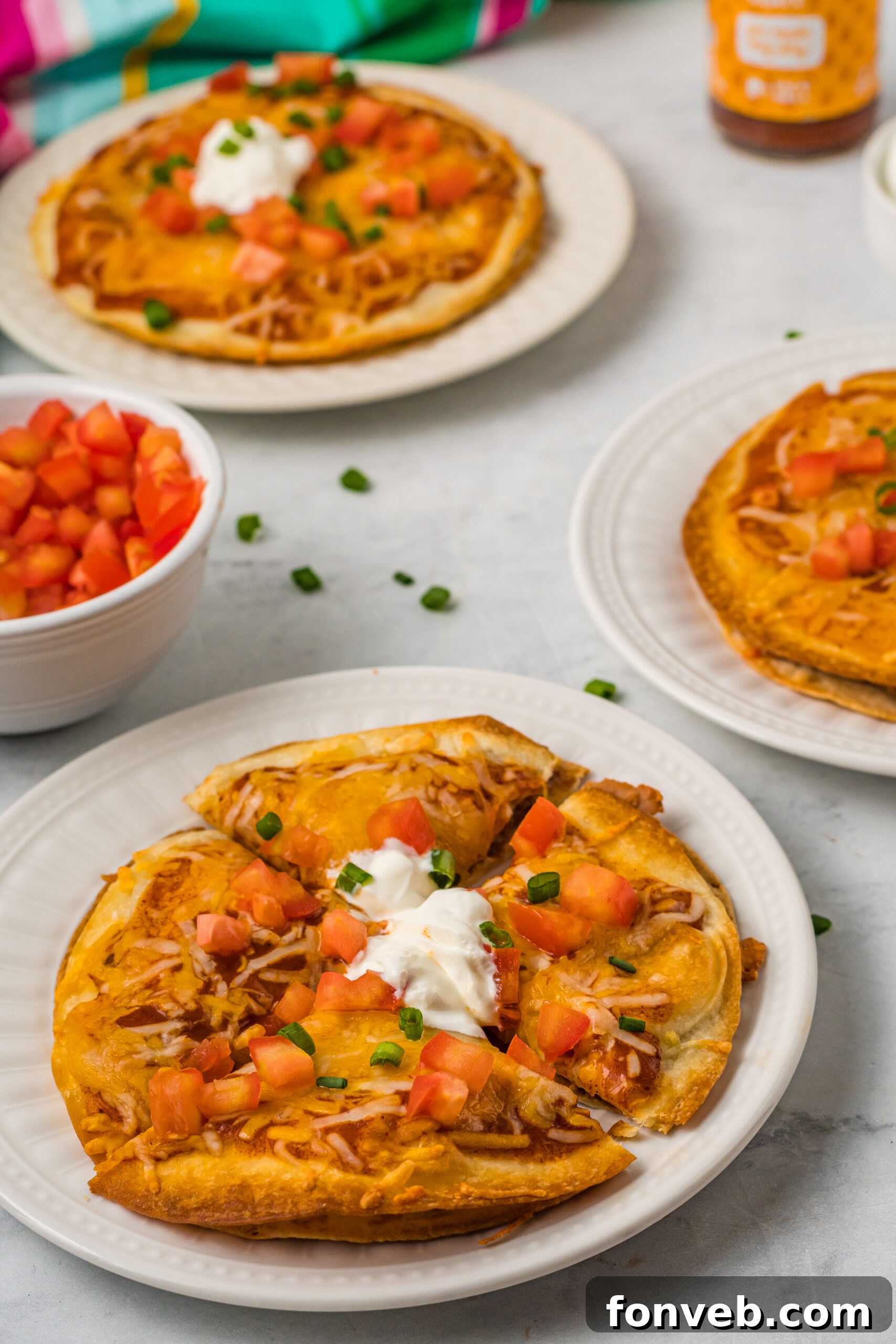 Mexican Pizza on a white plate cut into quarters topped with sour cream, tomatoes, and green onion. 