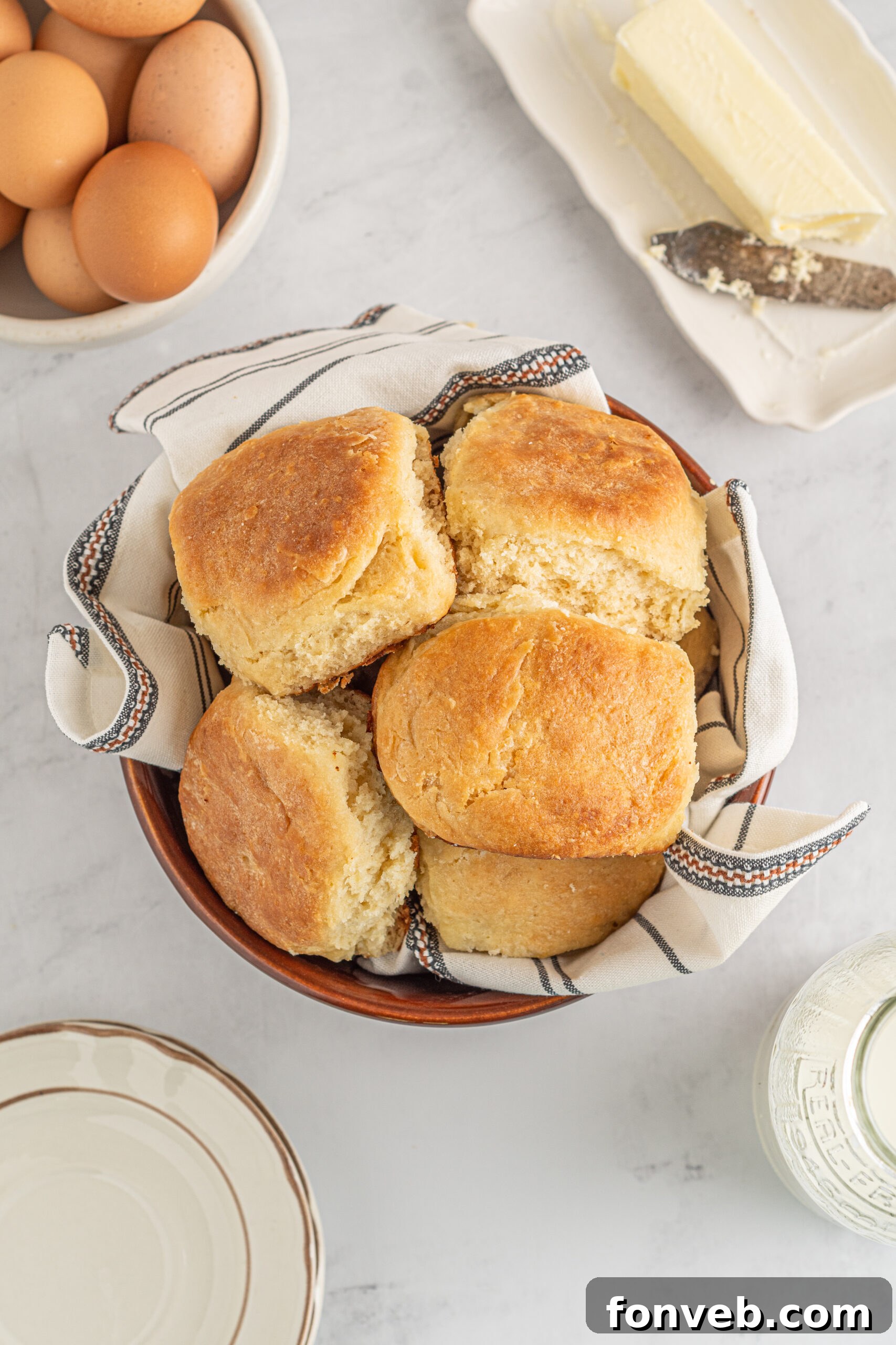 Freshly baked Angel Biscuits nestled in a rustic brown bowl, set against a charming white and black checkered linen, highlighting their golden tops.