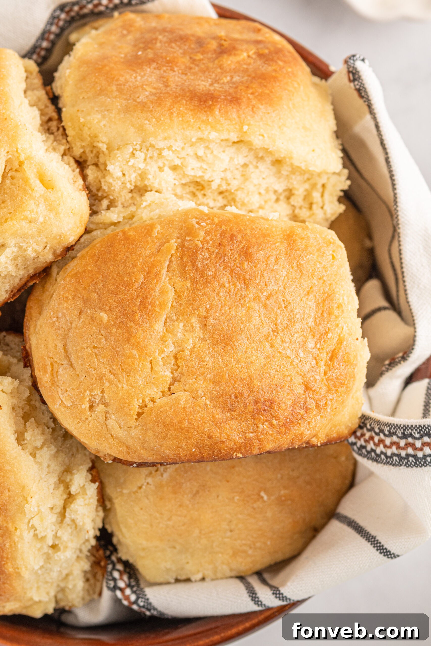 A detailed close-up shot of fluffy Angel Biscuits in a brown bowl with a white and black linen, emphasizing their soft texture and flaky layers.