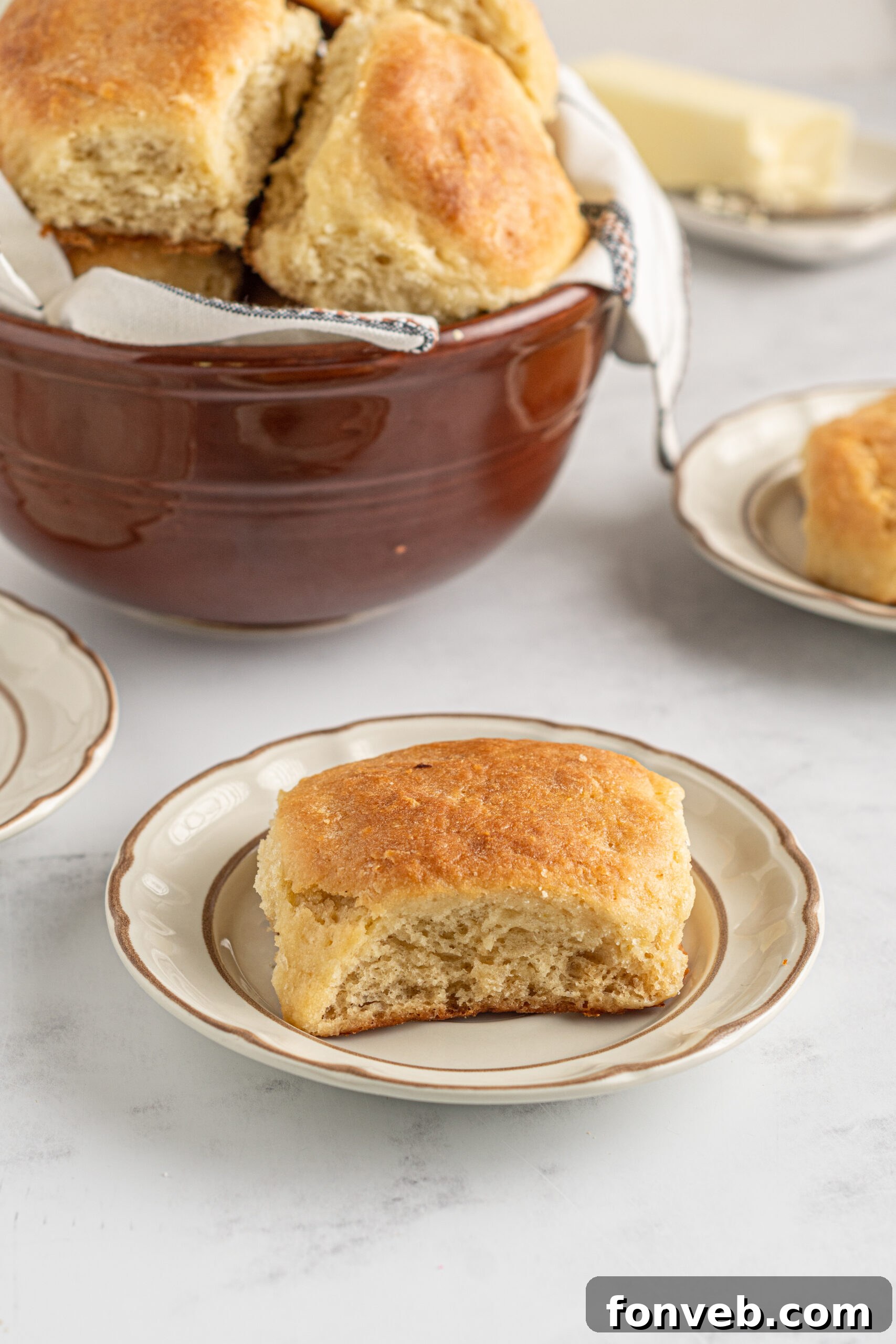 A single Angel Biscuit resting on a stylish tan and brown plate, with a bowl of more biscuits blurred in the background, creating an inviting scene.