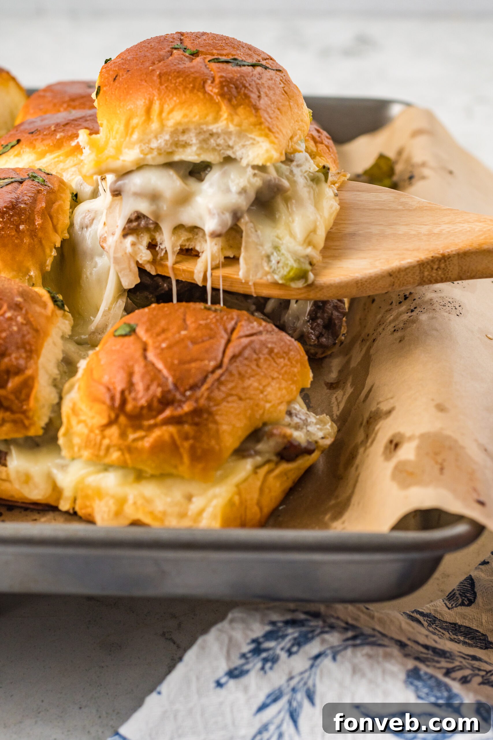 Ultimate Philly Cheesesteak Sliders 2 A Philly Cheesesteak Slider being removed from a baking sheet with a wooden spatula.