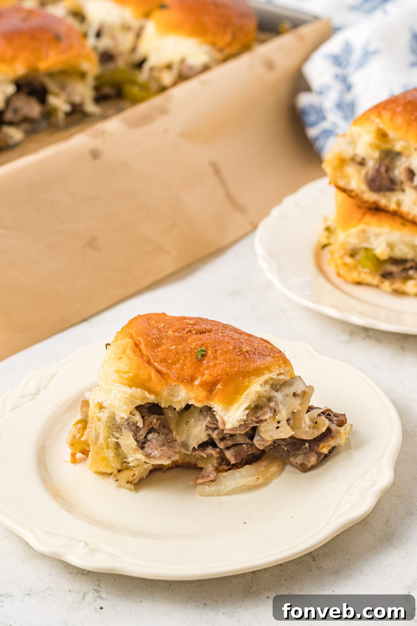 Ultimate Philly Cheesesteak Sliders 8 One slider on a white plate with a bite removed showing the cheesy inside.