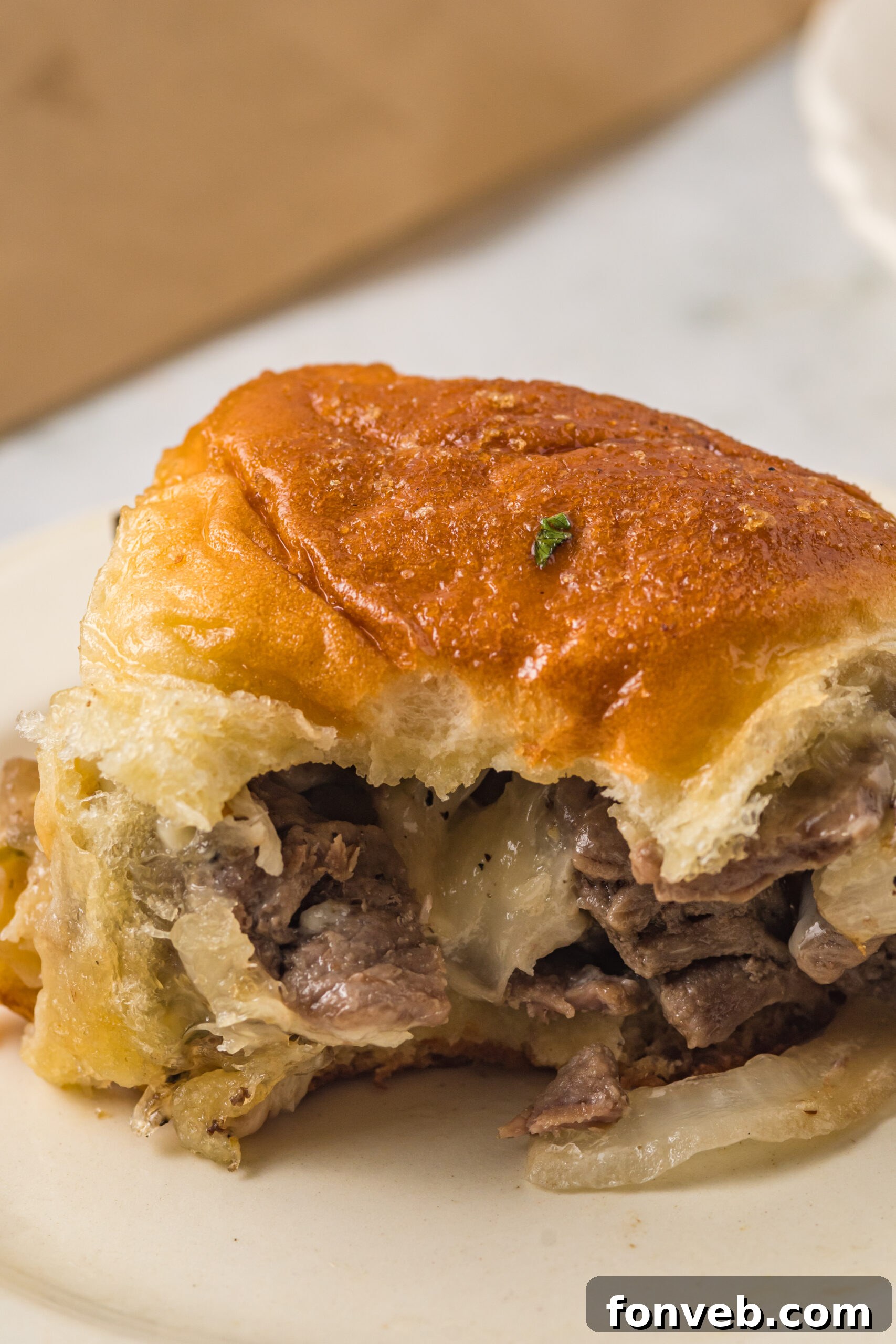 Ultimate Philly Cheesesteak Sliders 10 One slider on a white plate with a bite removed showing the inside.