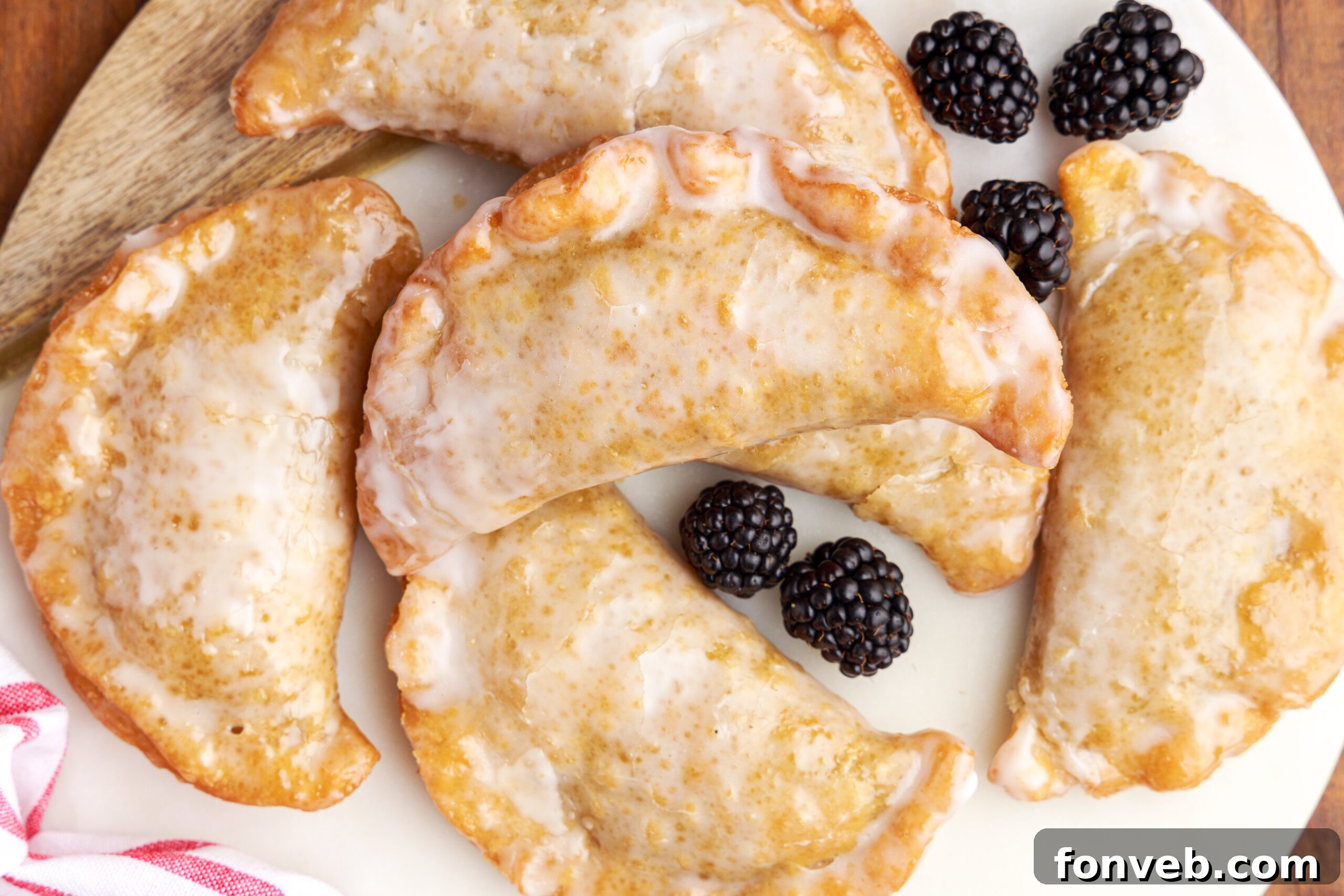 Overhead shot of blackberry hand pies stacked on a marble serving tray with fresh blackberries.