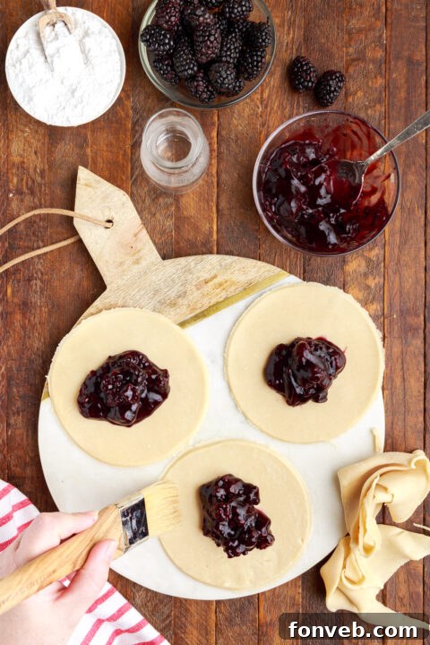 three circle of pie dough on a marble serving tray with blackberry jam in the center of each circle.