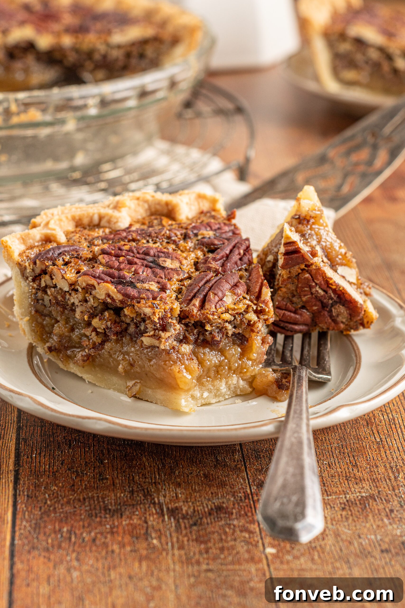 Bourbon Pecan Indulgence 14 A piece of pecan pie on a tan and brown plate with a bite of pie being removed with a silver fork.