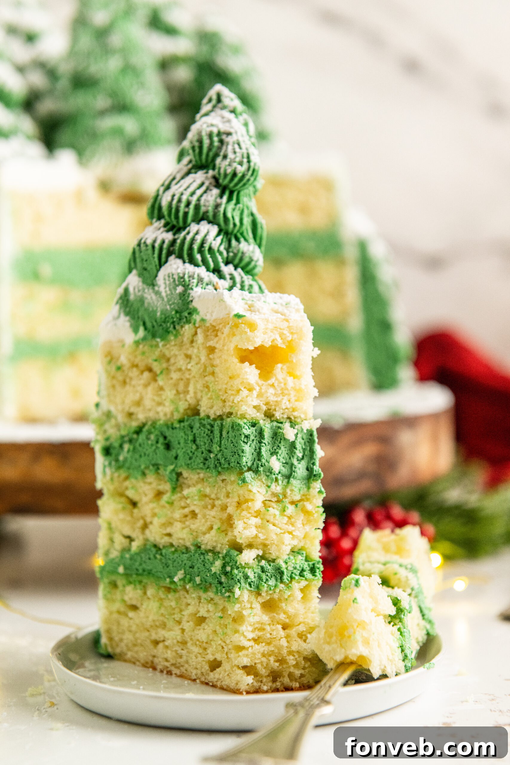 A shot of a piece of Christmas tree cake on a white plate  with a bite removed onto a silver fork and placed to the side. 