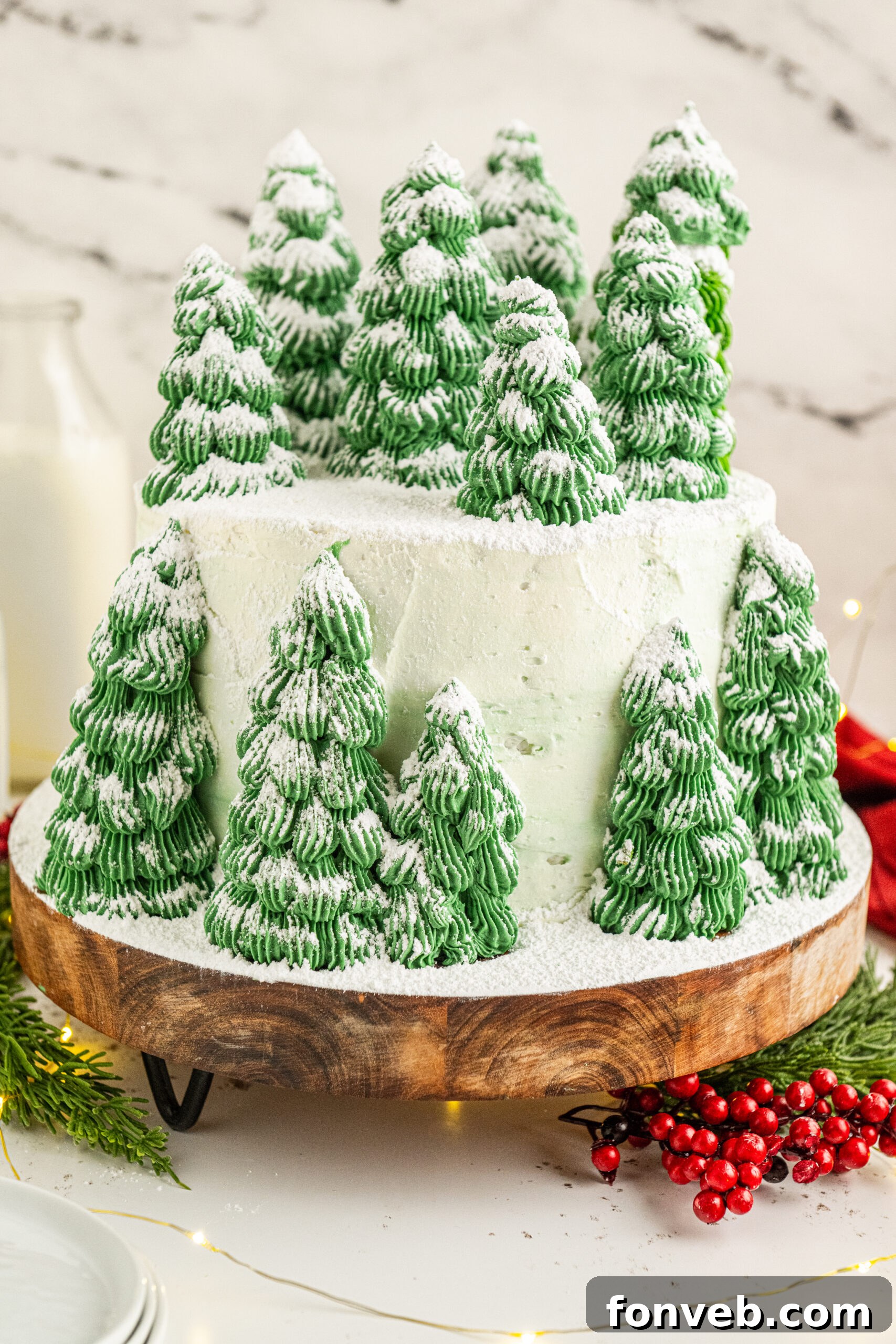A white cake with green Christmas tree cones, sprinkled with powdered sugar. 