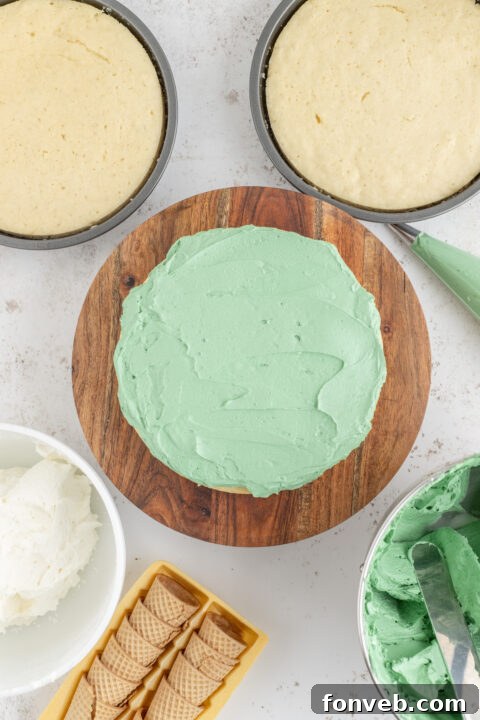 A hand piping green frosting onto a sugar cone.