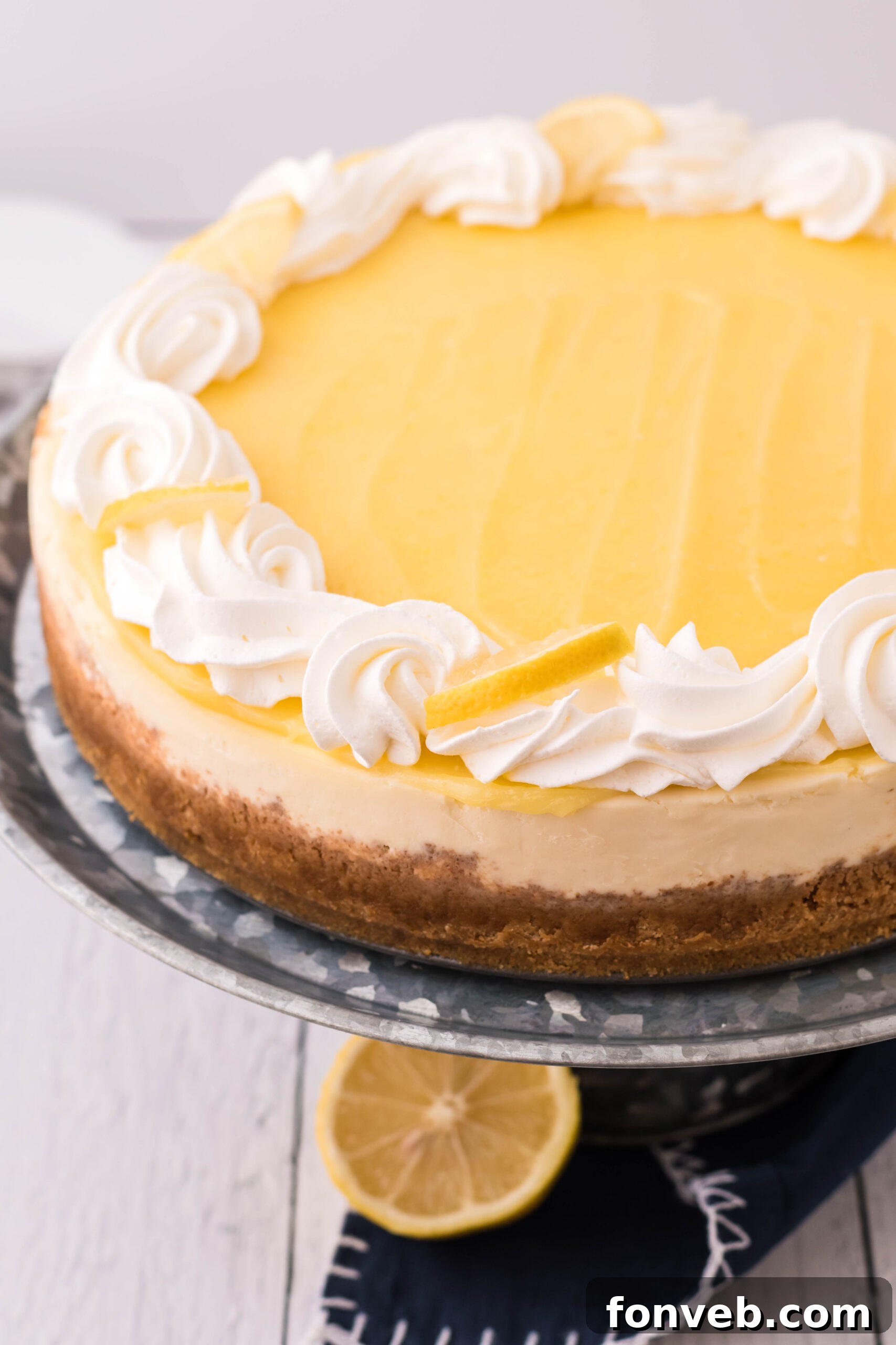 Lemon Curd Cheesecake topped with whipped cream and lemon slices on a metal serving stand.