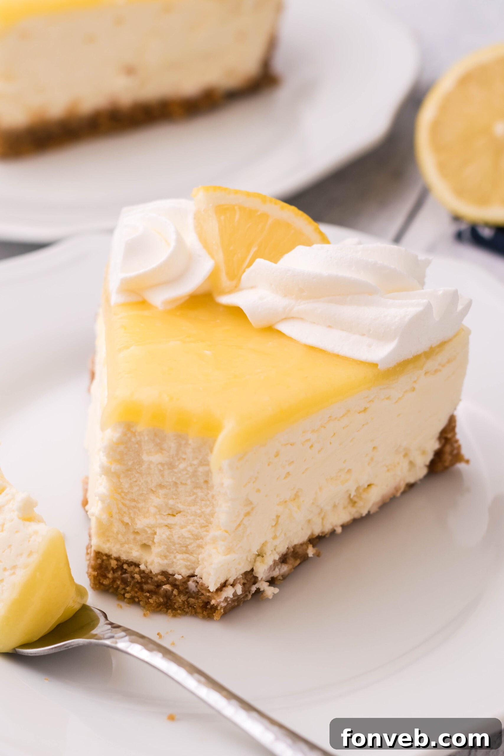 A slice of cheesecake topped with whipped cream and a lemon slice on a white plate with a bite removed.