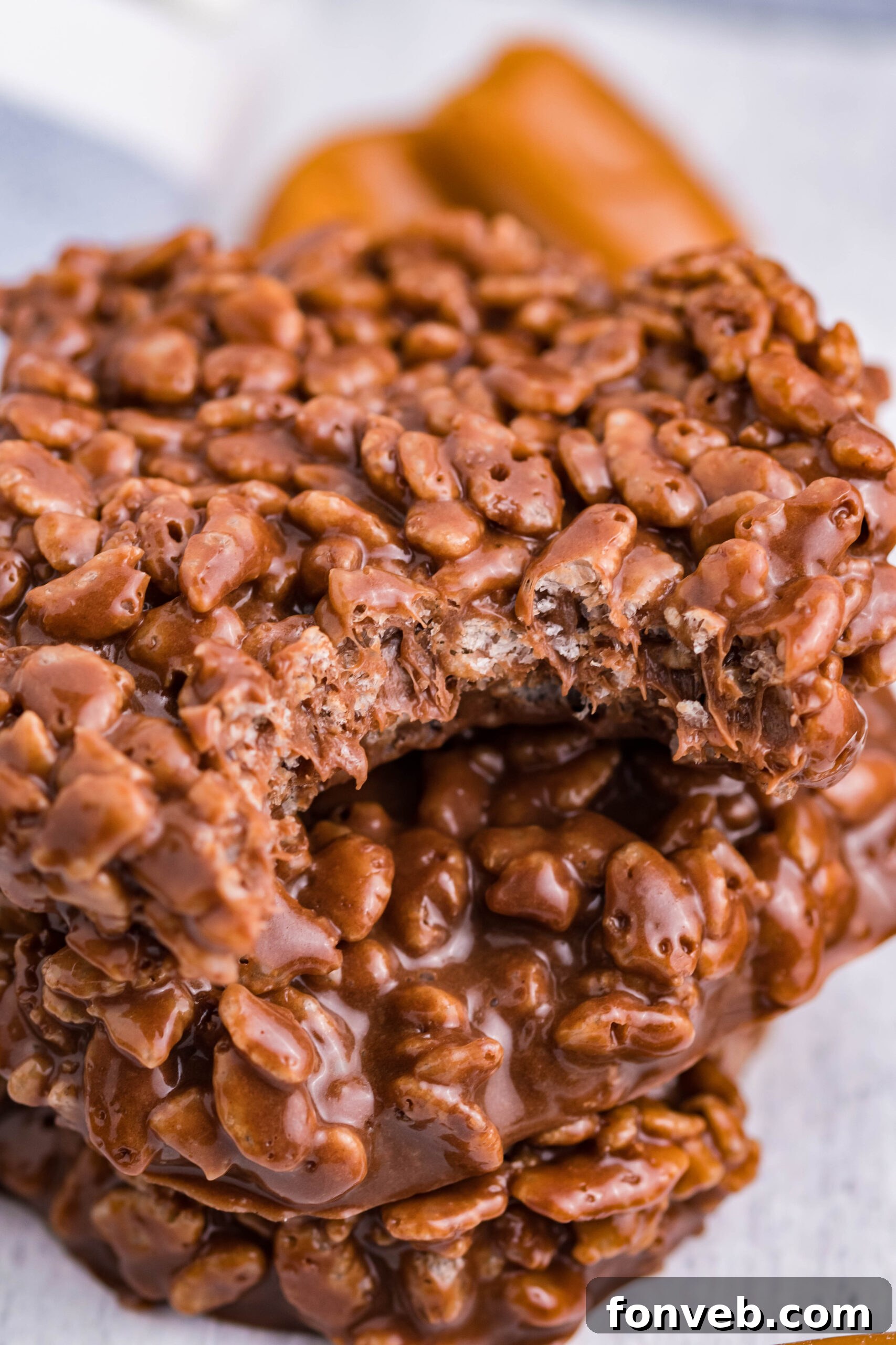Three perfectly stacked homemade Star Crunch copycat cookies, glistening with chocolate and caramel, presented on a distressed white wooden surface, with a bite taken from the top cookie to reveal its tempting layers.