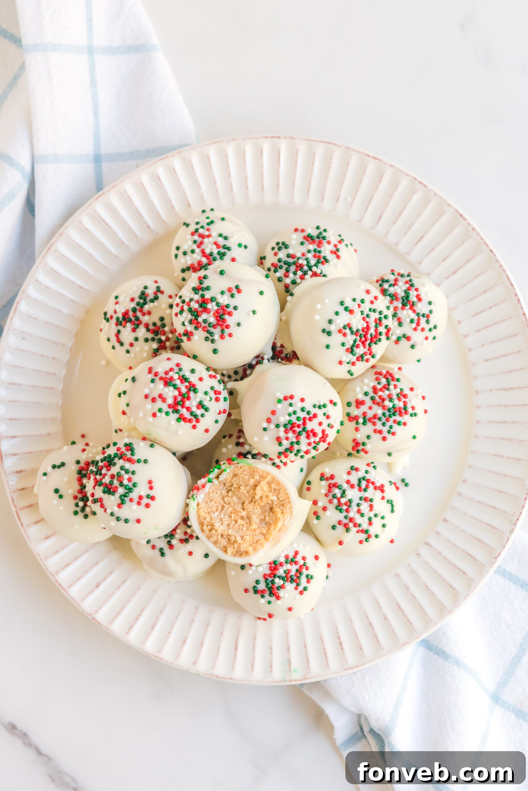 Overhead view of White Chocolate Truffles stacked on a white plate topped with red, white, and green sprinkles. 