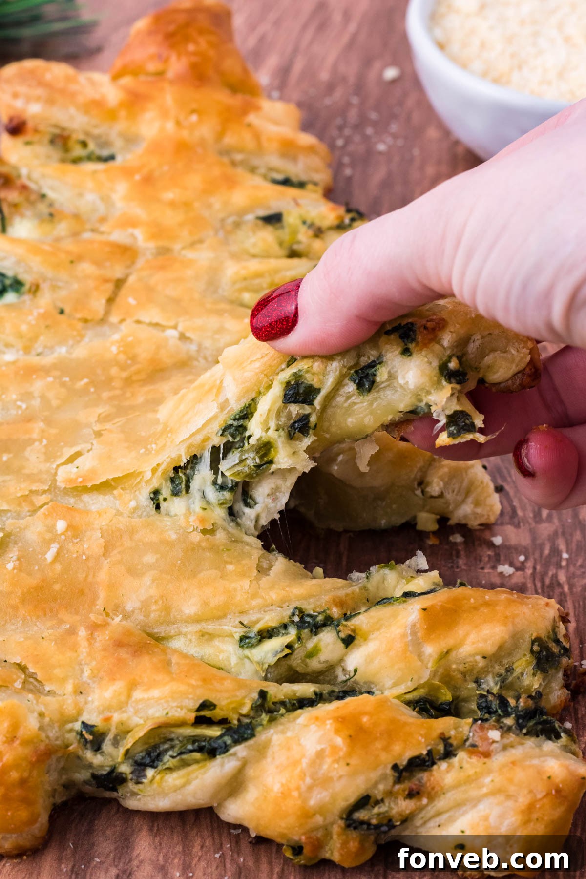 Tear and Share Christmas Spinach Artichoke Bread 4 Close-up photo of a hand pulling a piece of the warm Spinach Artichoke Dip Christmas Tree Bread, revealing the creamy, cheesy spinach artichoke filling within.