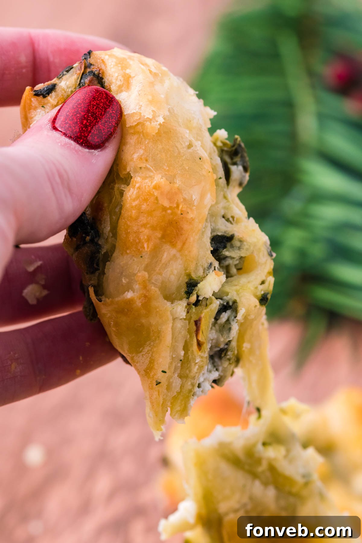 Tear and Share Christmas Spinach Artichoke Bread 7 A hand holding up a piece of the pull-apart bread, showcasing its flaky puff pastry layers and inviting cheesy spinach artichoke filling.