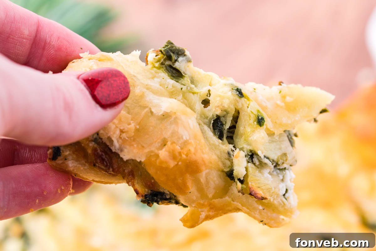 Tear and Share Christmas Spinach Artichoke Bread 9 A close-up view of a piece of the Spinach Artichoke Dip Pull Apart Christmas Tree Bread being held, highlighting its flaky exterior and generous, warm spinach dip filling.