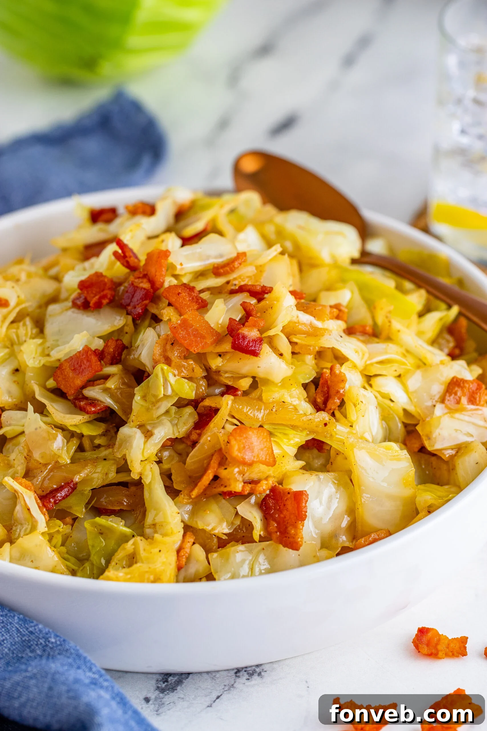 Bacon Fried Cabbage in a white bowl topped with bacon with a gold spoon on the side