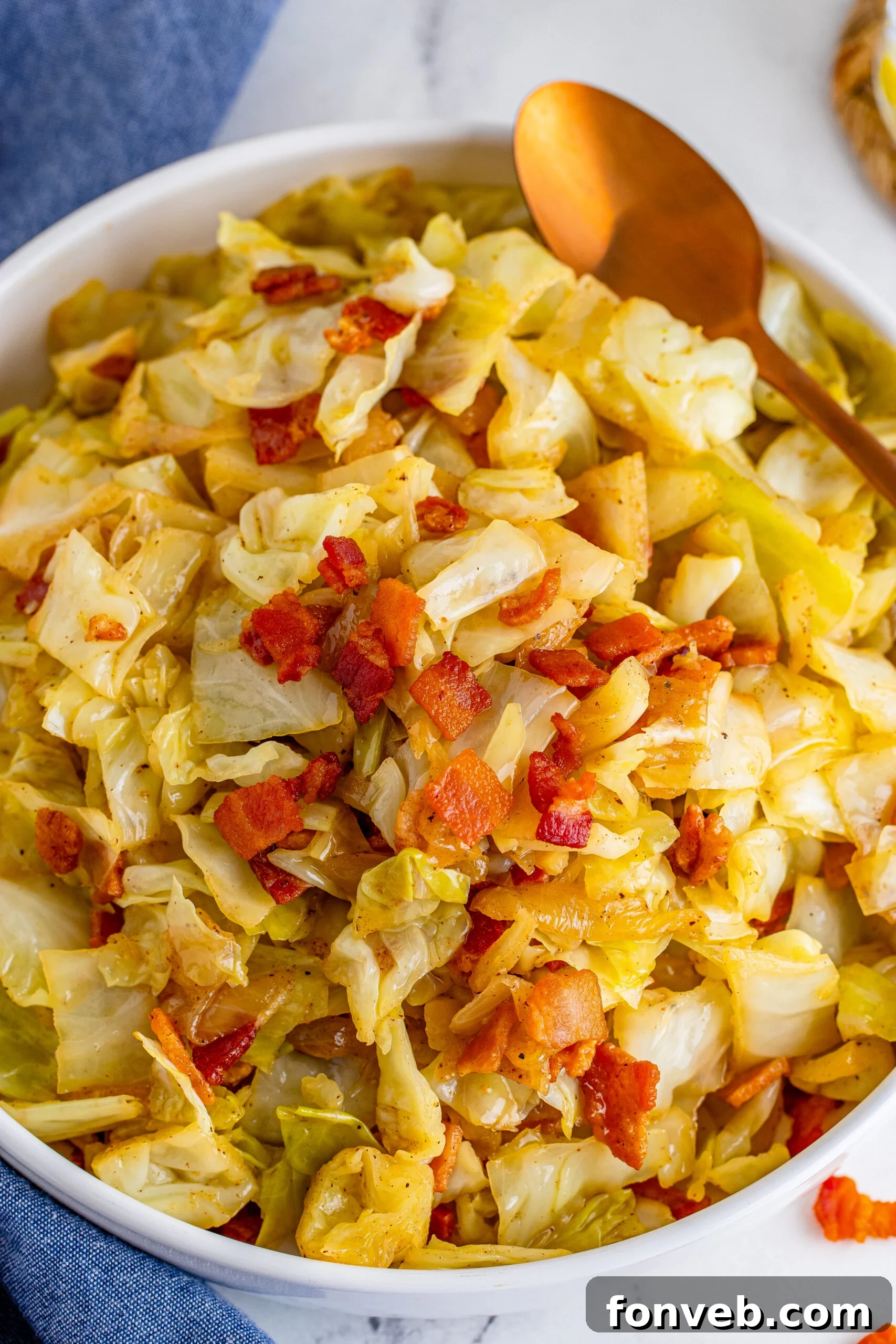 Bacon Fried Cabbage in a white bowl topped with bacon with a gold spoon on the side