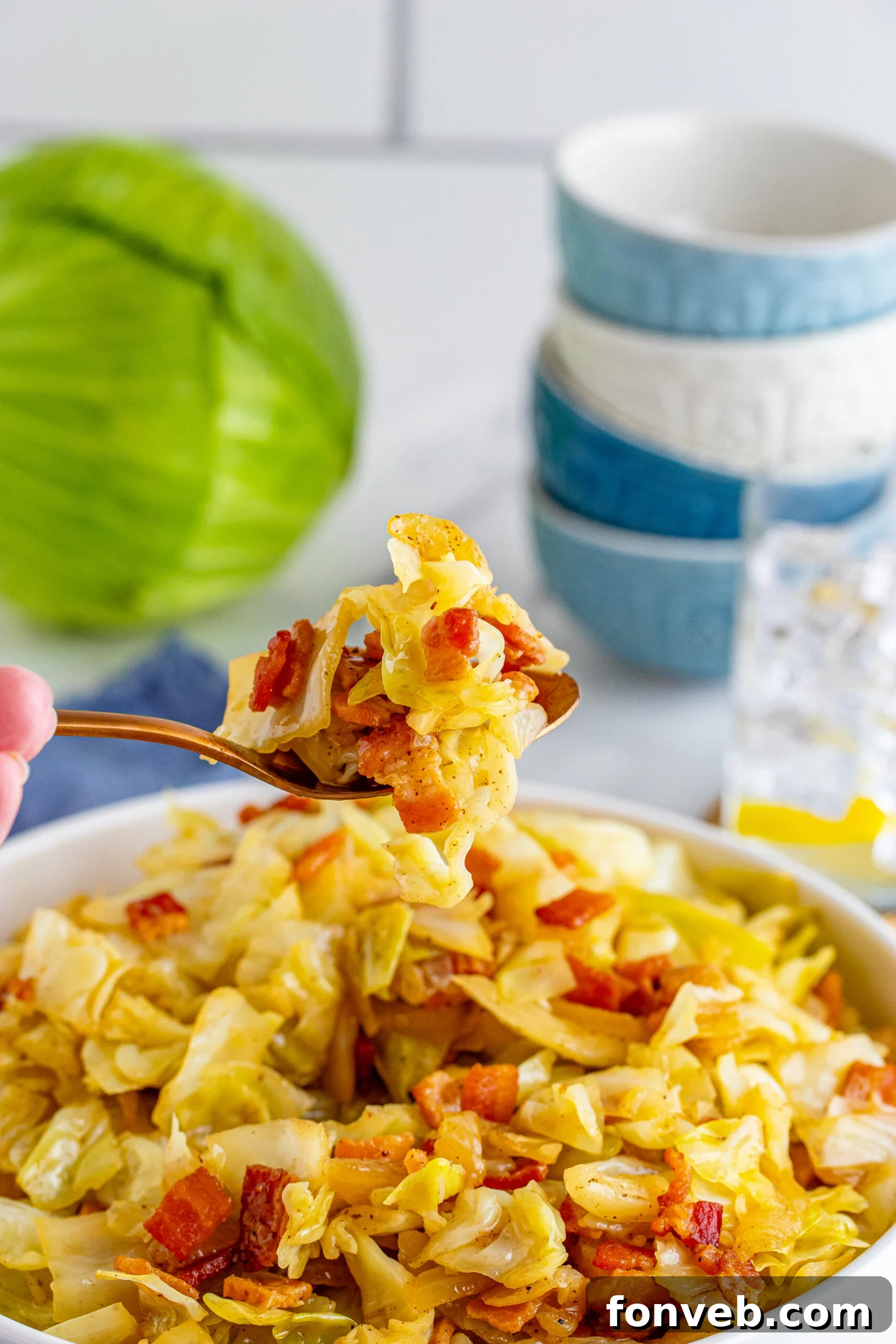 Fried Cabbage in a white bowl with a bite being removed with a gold spoon. 
